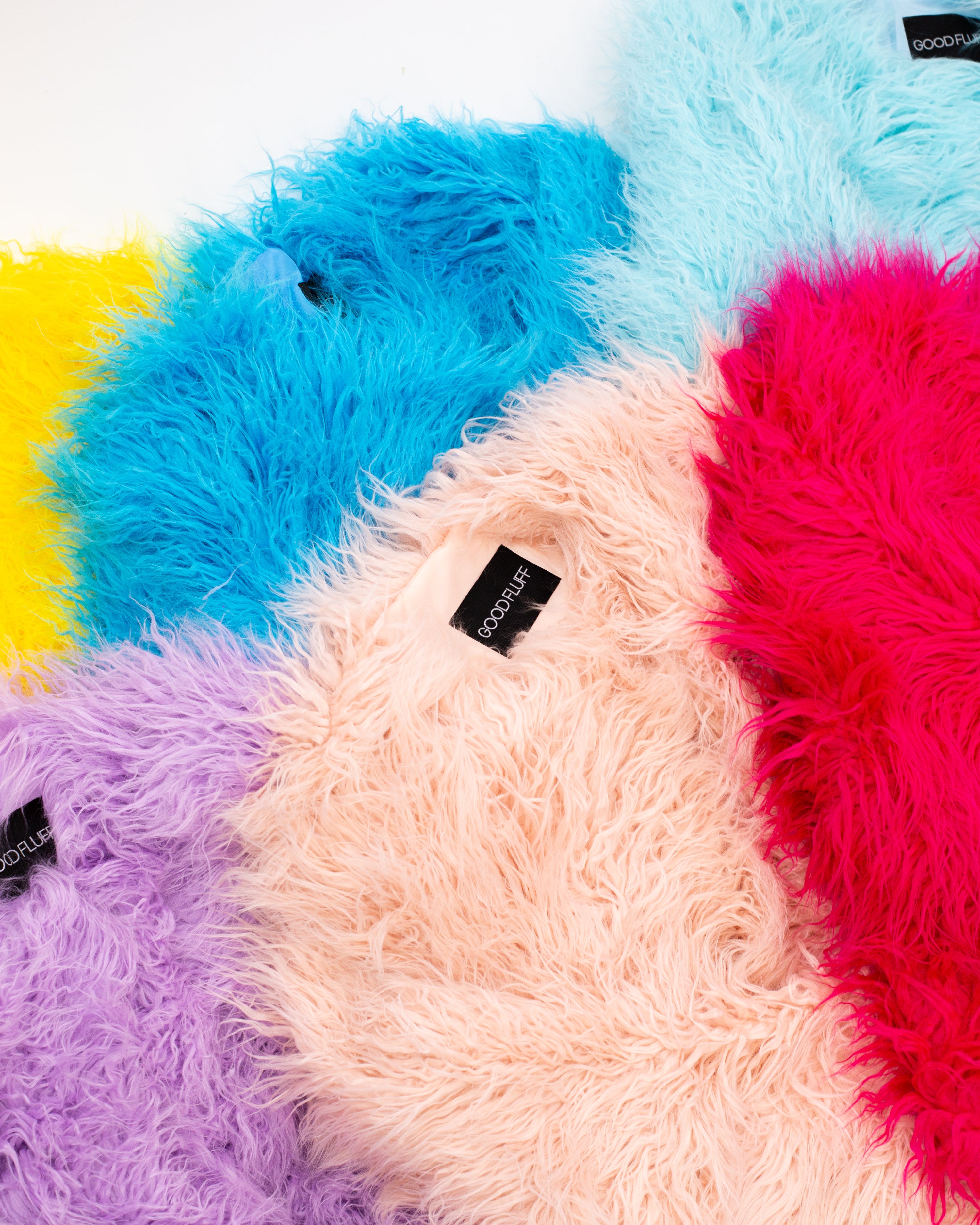 Multicoloured fluffy faux fur jackets with visible brand labels on a white background