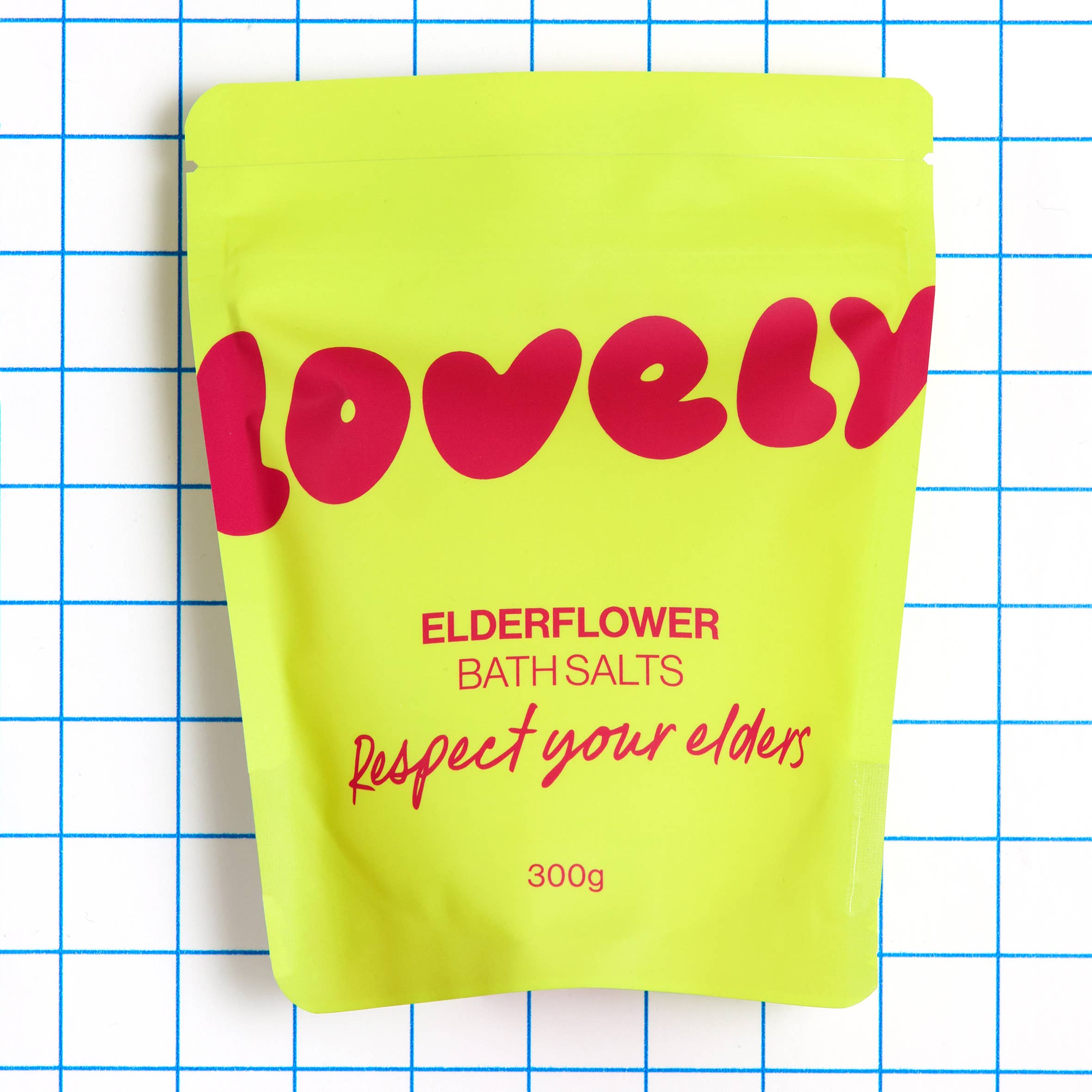 Yellow package of 'Lovely' elderflower bath salts with red text on a grid background