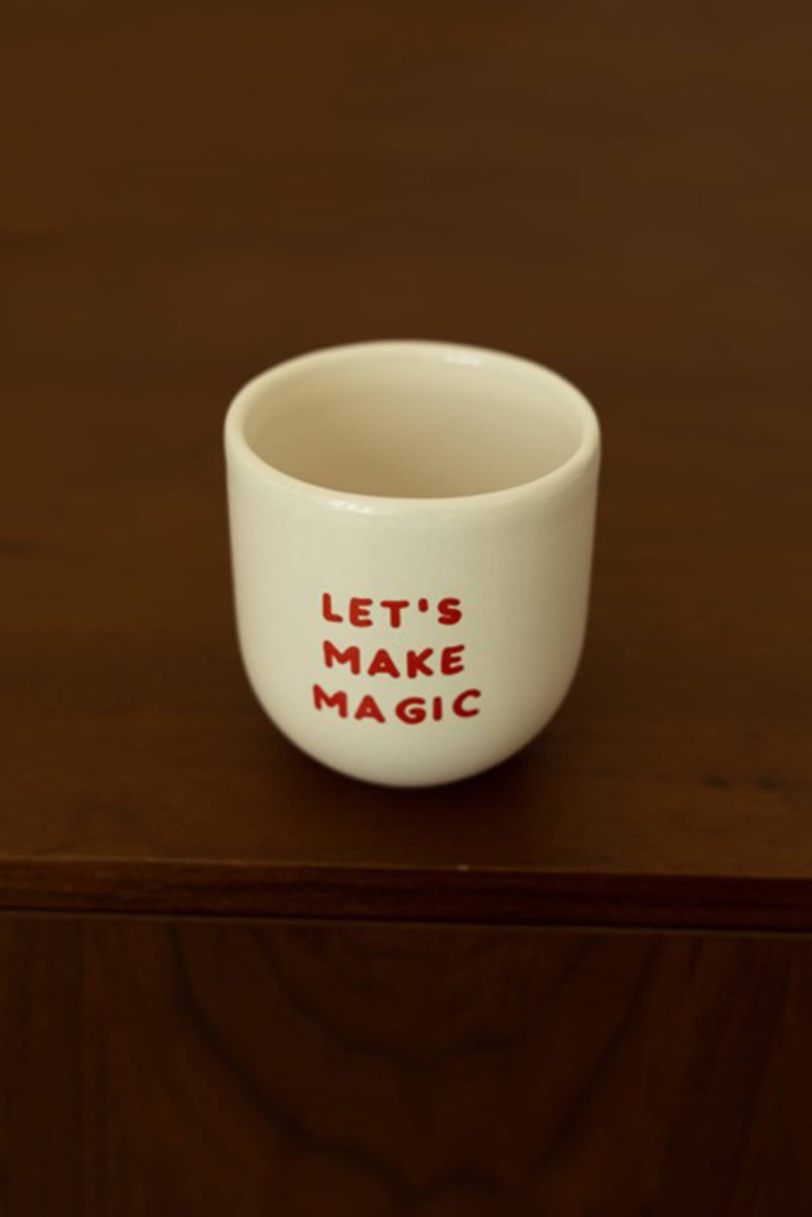 White ceramic cup with 'LET'S MAKE MAGIC' text on a brown surface