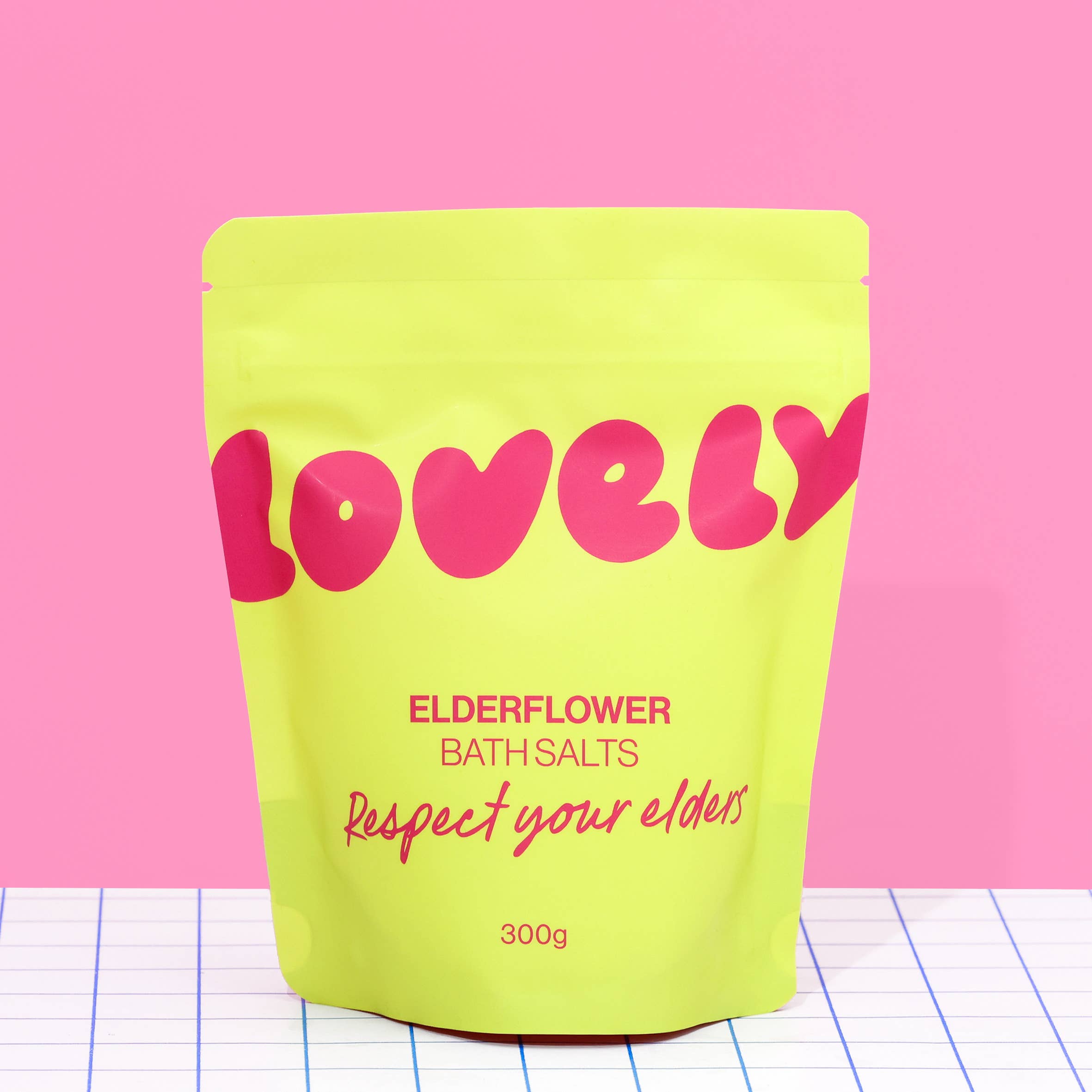 Yellow package of 'Lovely' elderflower bath salts with pink text on a pink background