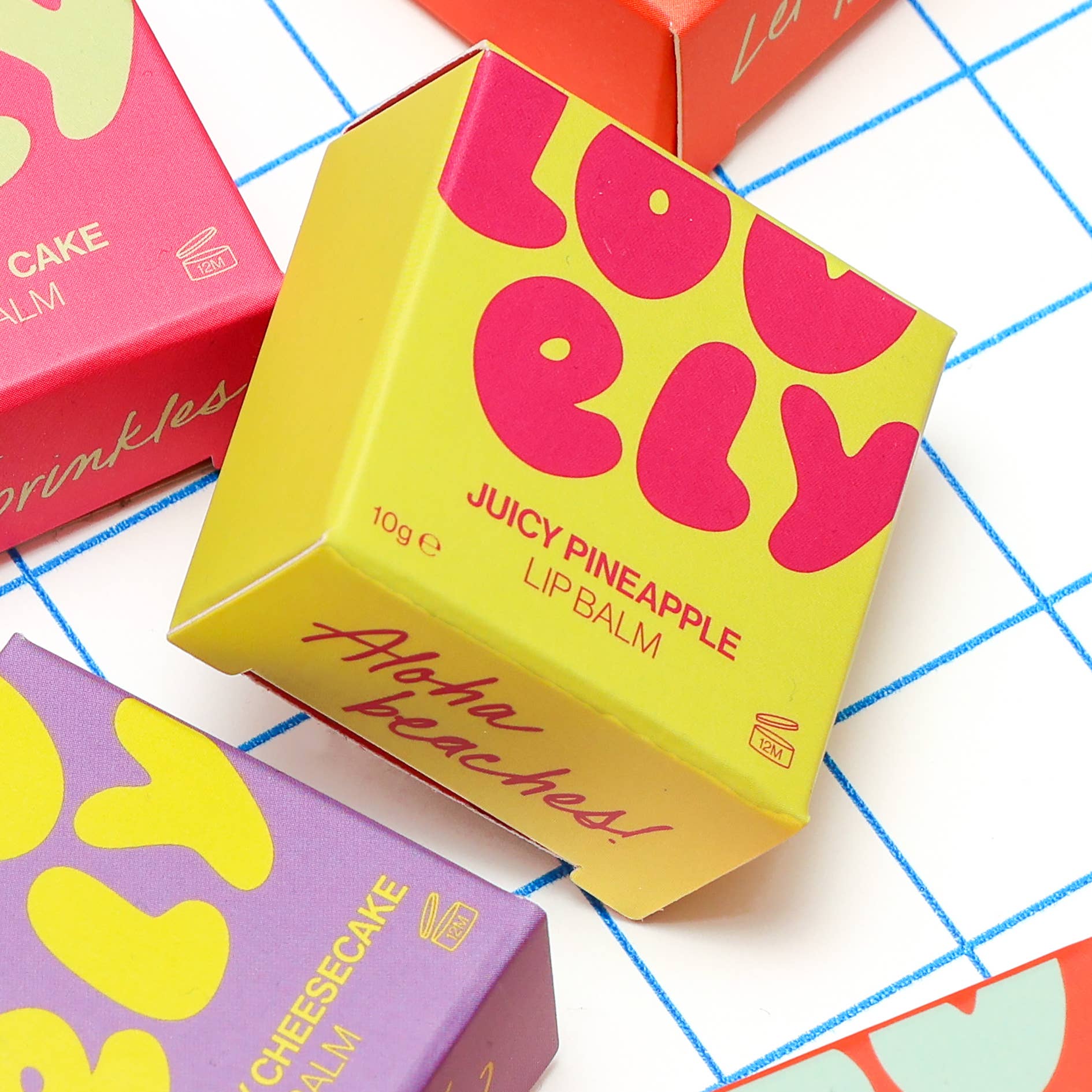 Colorful lip balm packaging with 'Juicy Pineapple' and 'Cheesecake' text on a patterned background
