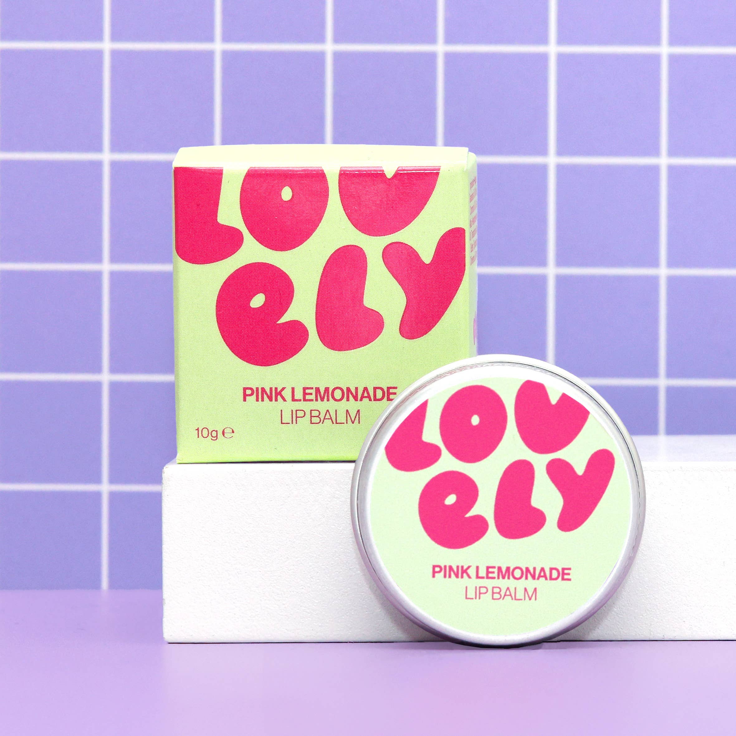 Pink Lemonade lip balm with packaging on a purple grid background