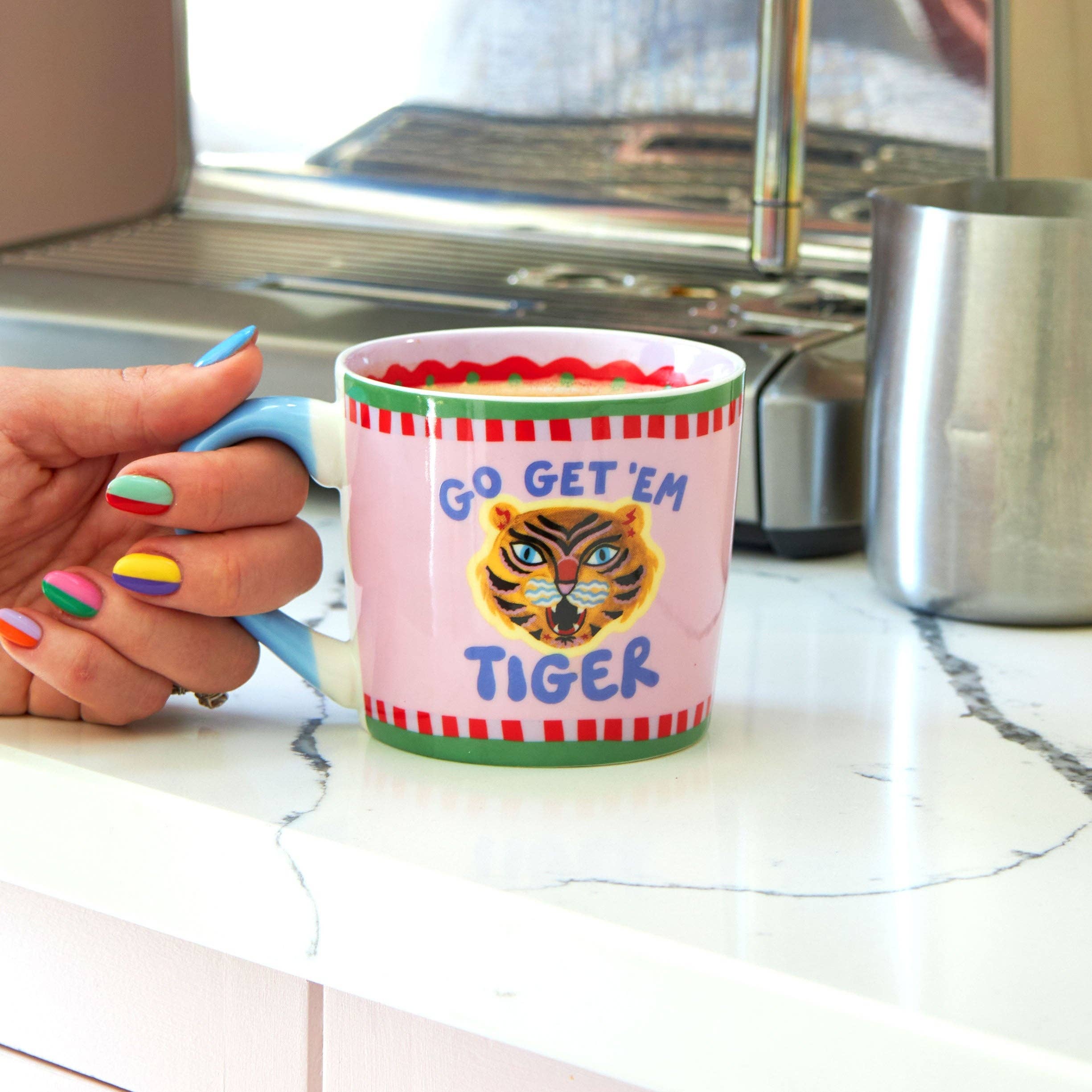 Person holding a mug with 'Go Get 'Em Tiger' design in a kitchen setting