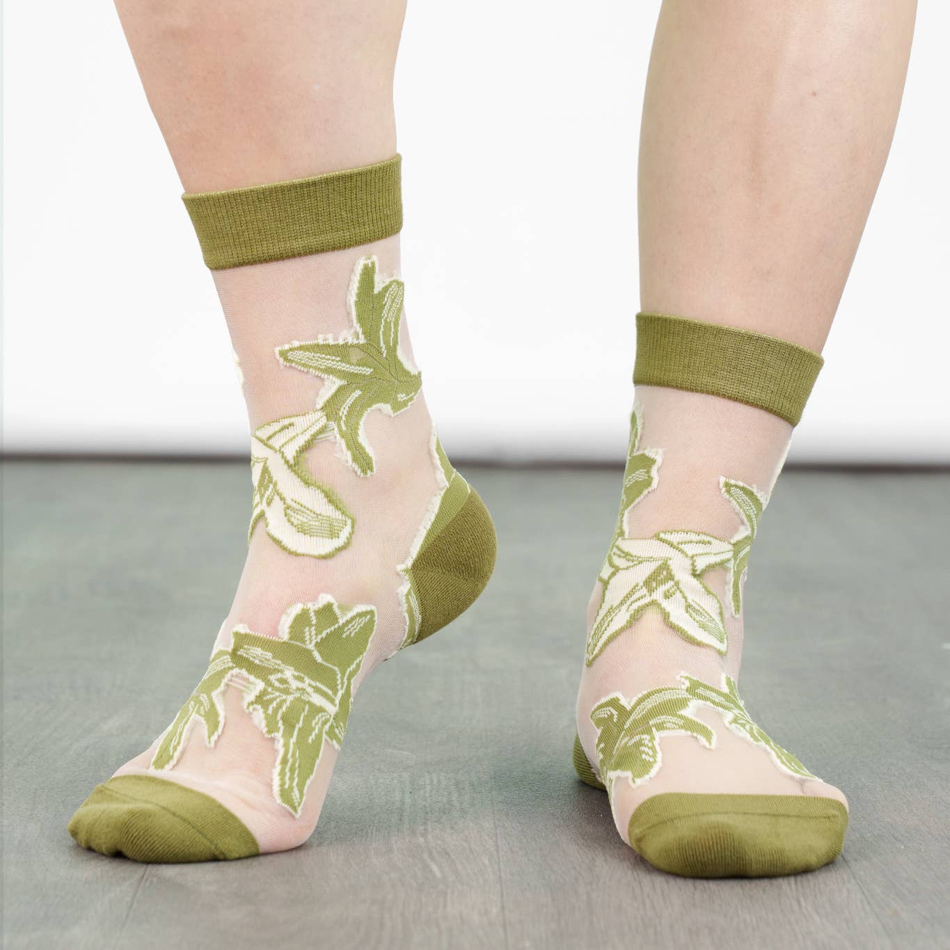 Sheer socks with green floral patterns and green cuffs and toes worn by a person.
