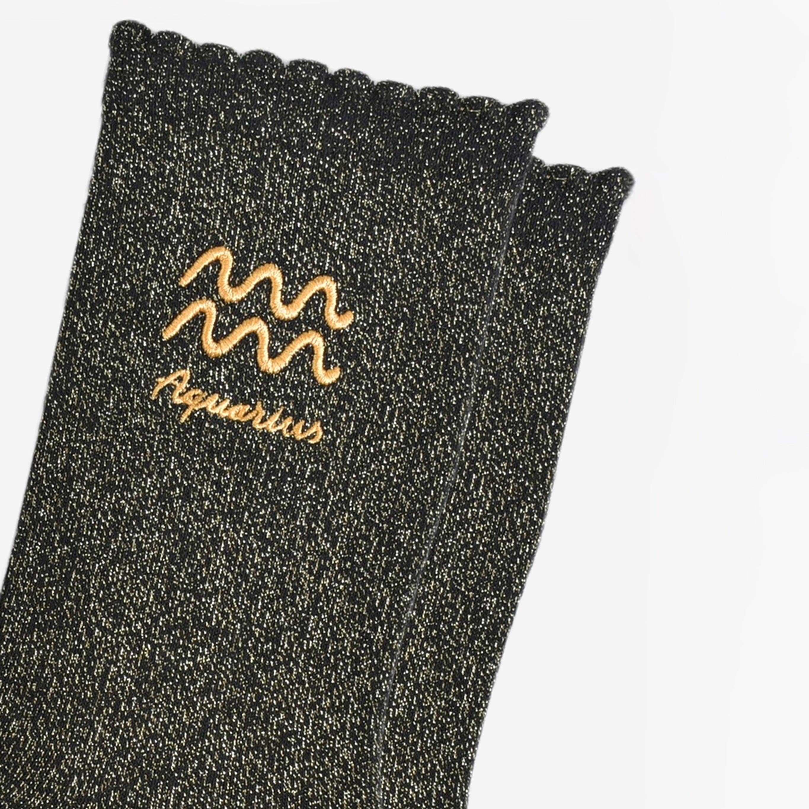 Black glittery sock with Aquarius zodiac sign embroidery on a light gray background