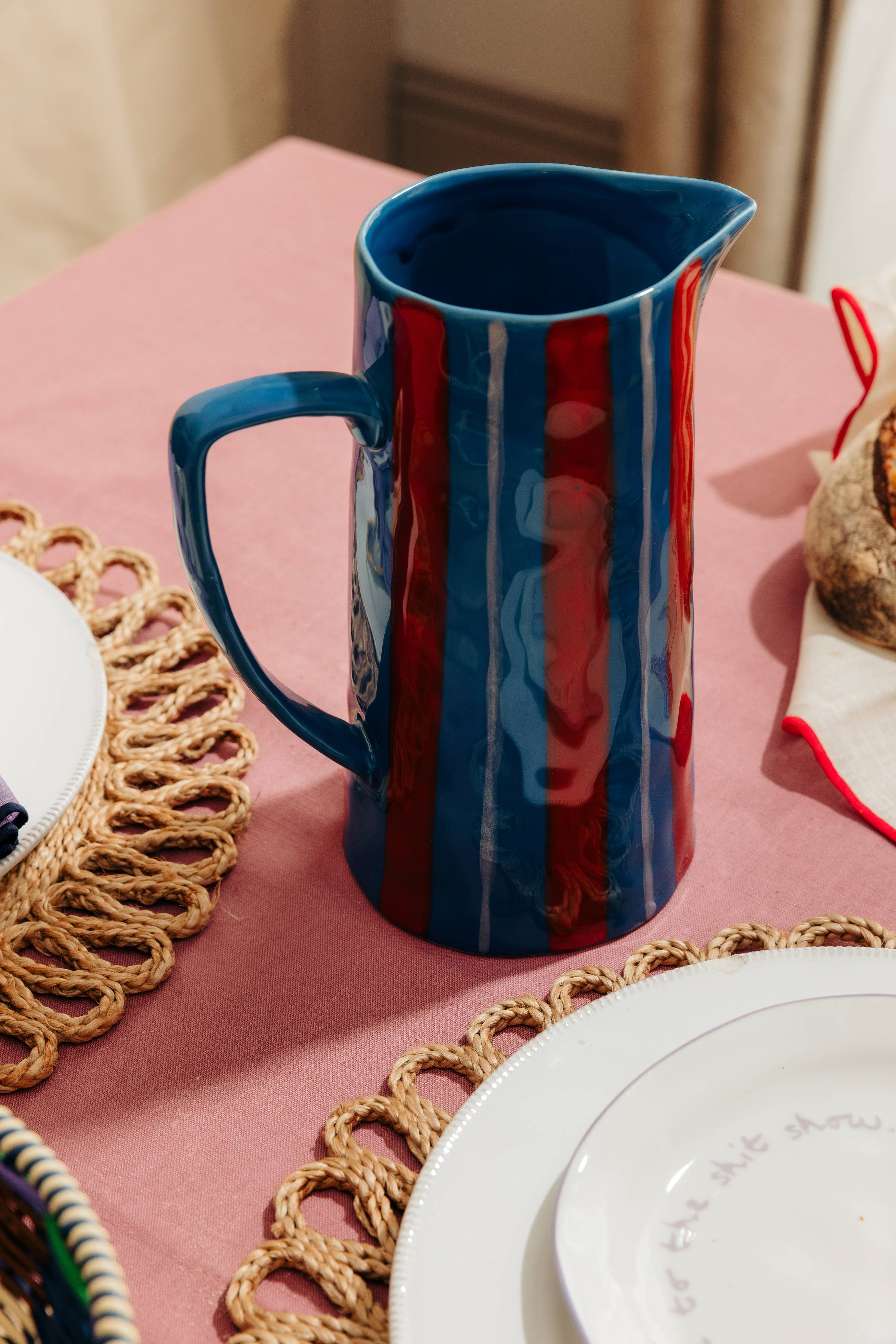 Blue ceramic pitcher on a pink tablecloth with decorative plates and placemats.
