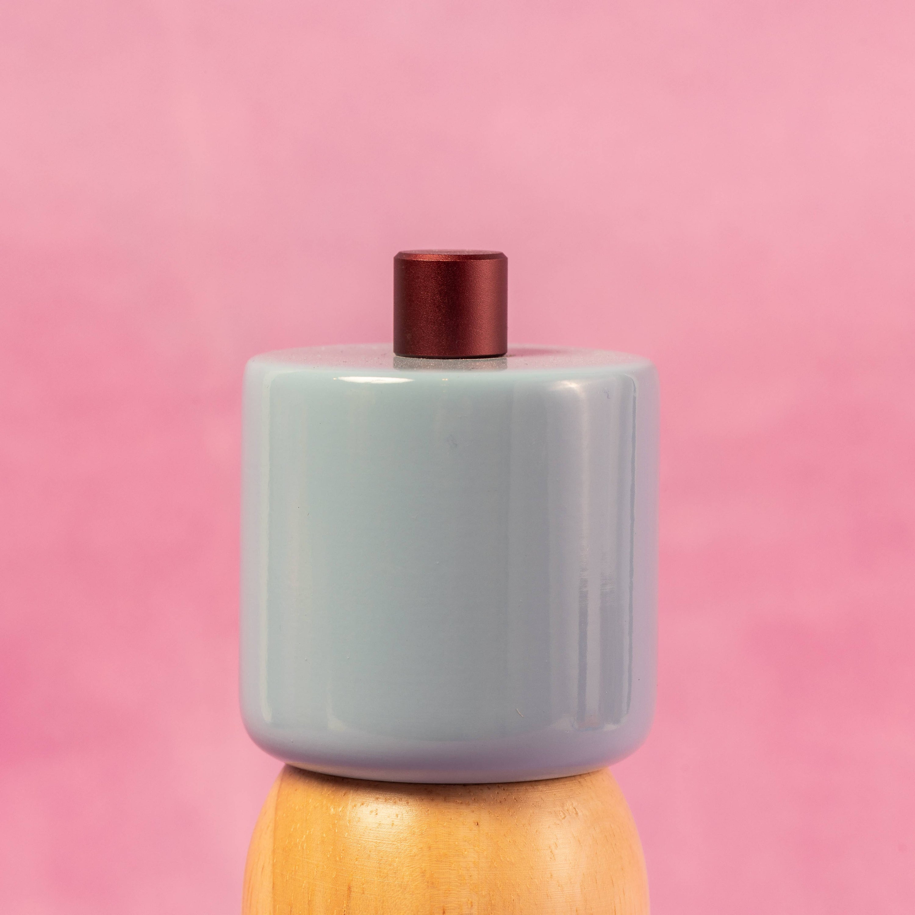 Cylindrical ceramic container with a red top on a wooden base against a pink background