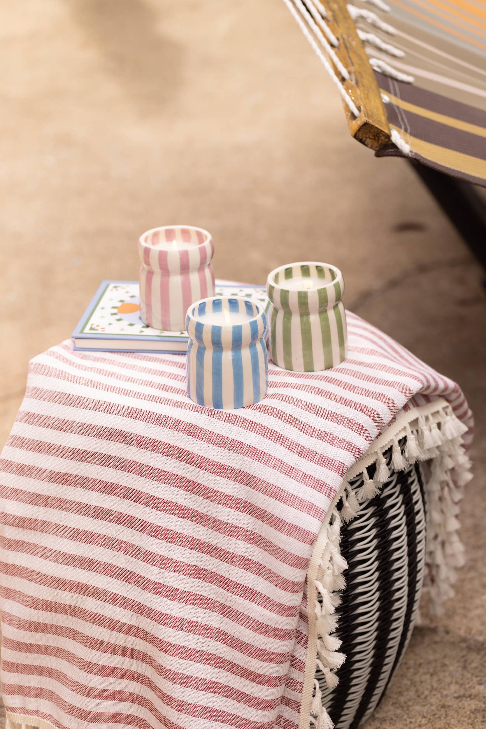Decorative stool with a striped pink and white cover, holding colorful vases and a book.
