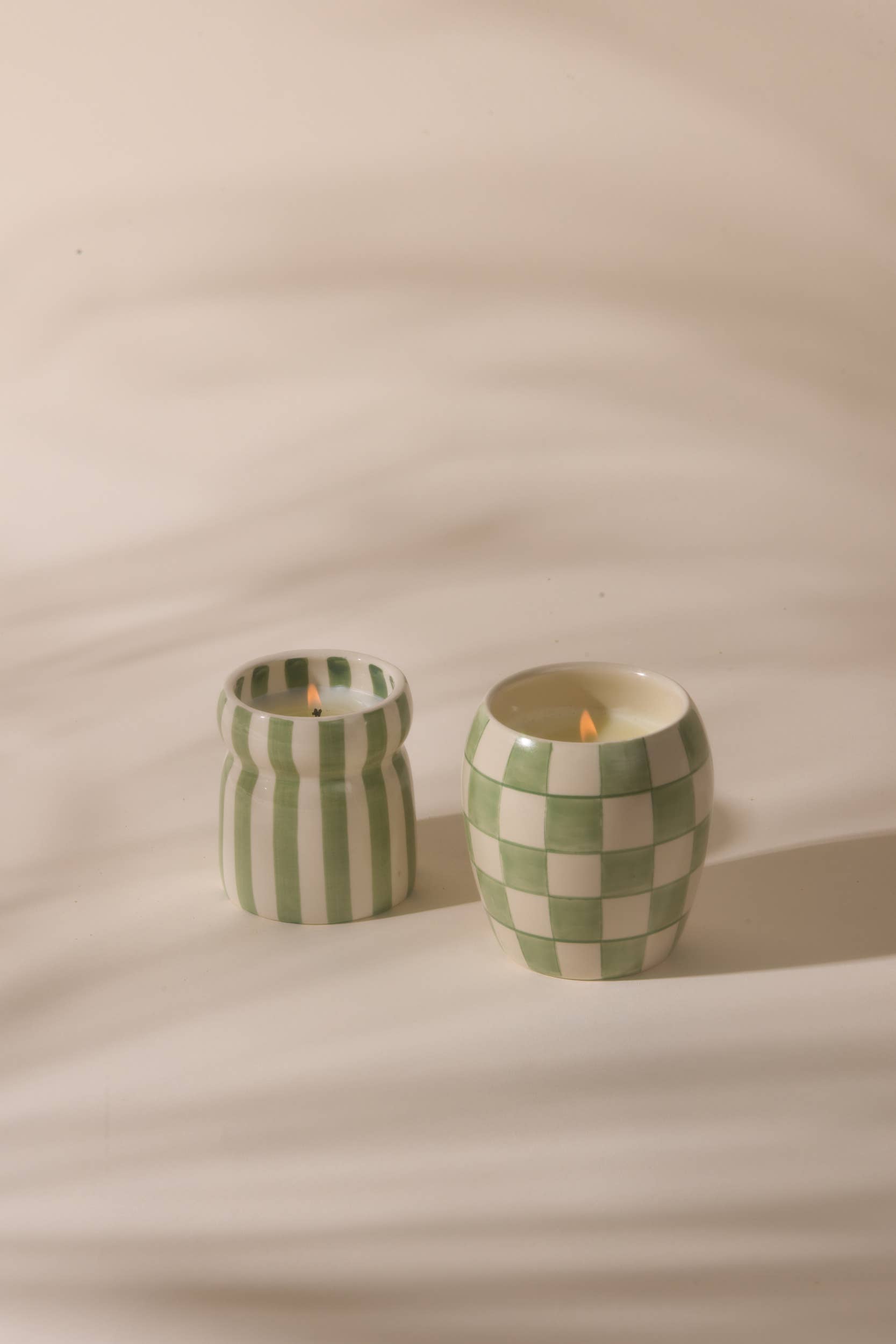 Two checkered candles in jars on a beige background
