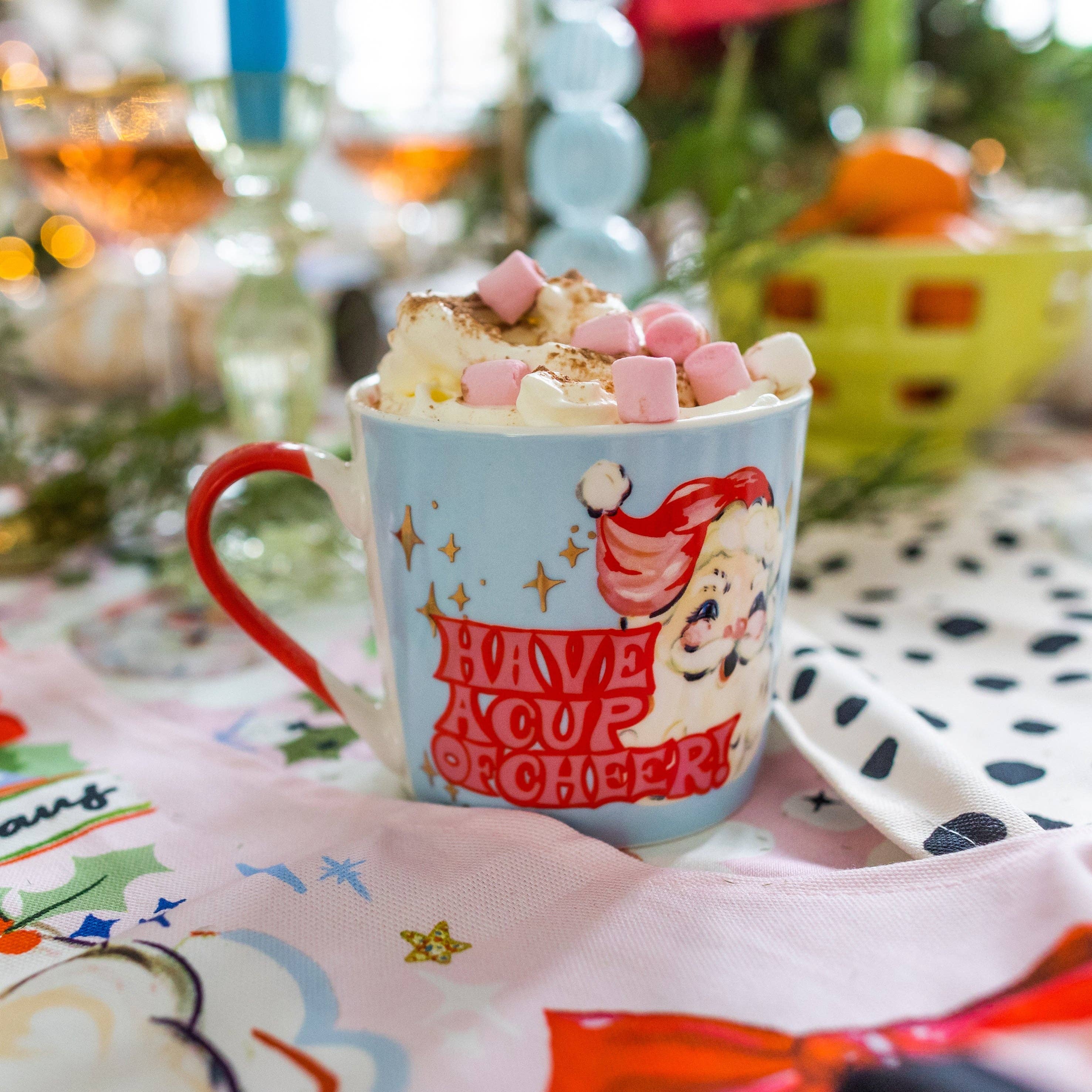 Mug with Santa design and hot chocolate with marshmallows on a festive table.