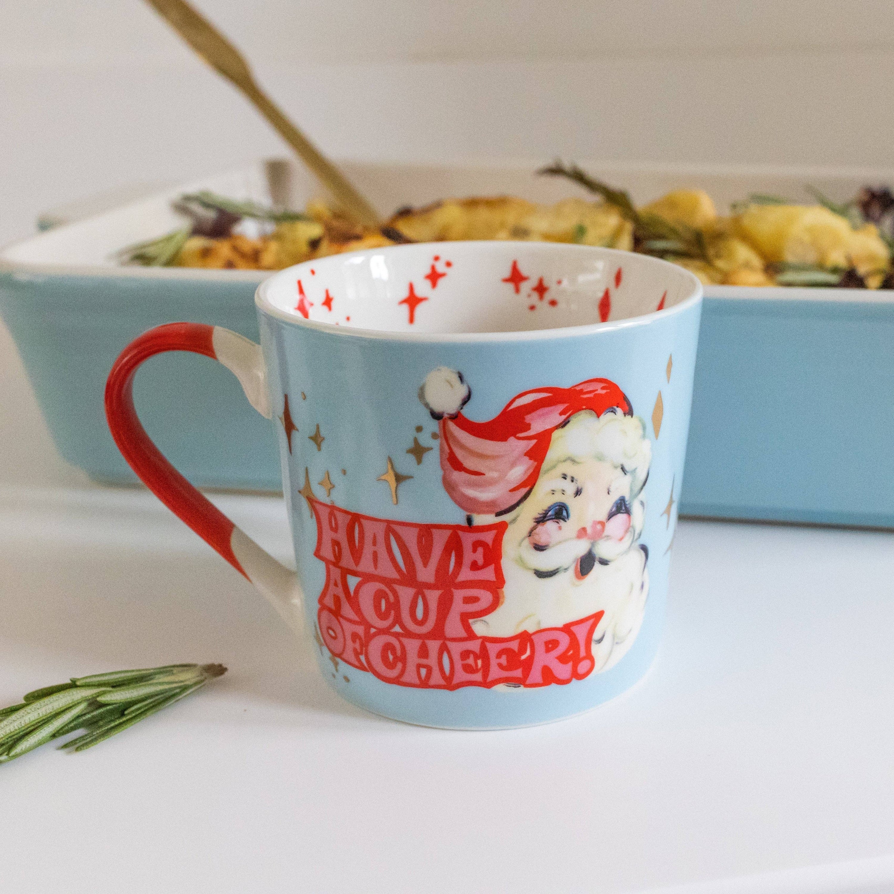 Mug with Santa design and 'Have a Cup of Cheer' text on a kitchen counter.