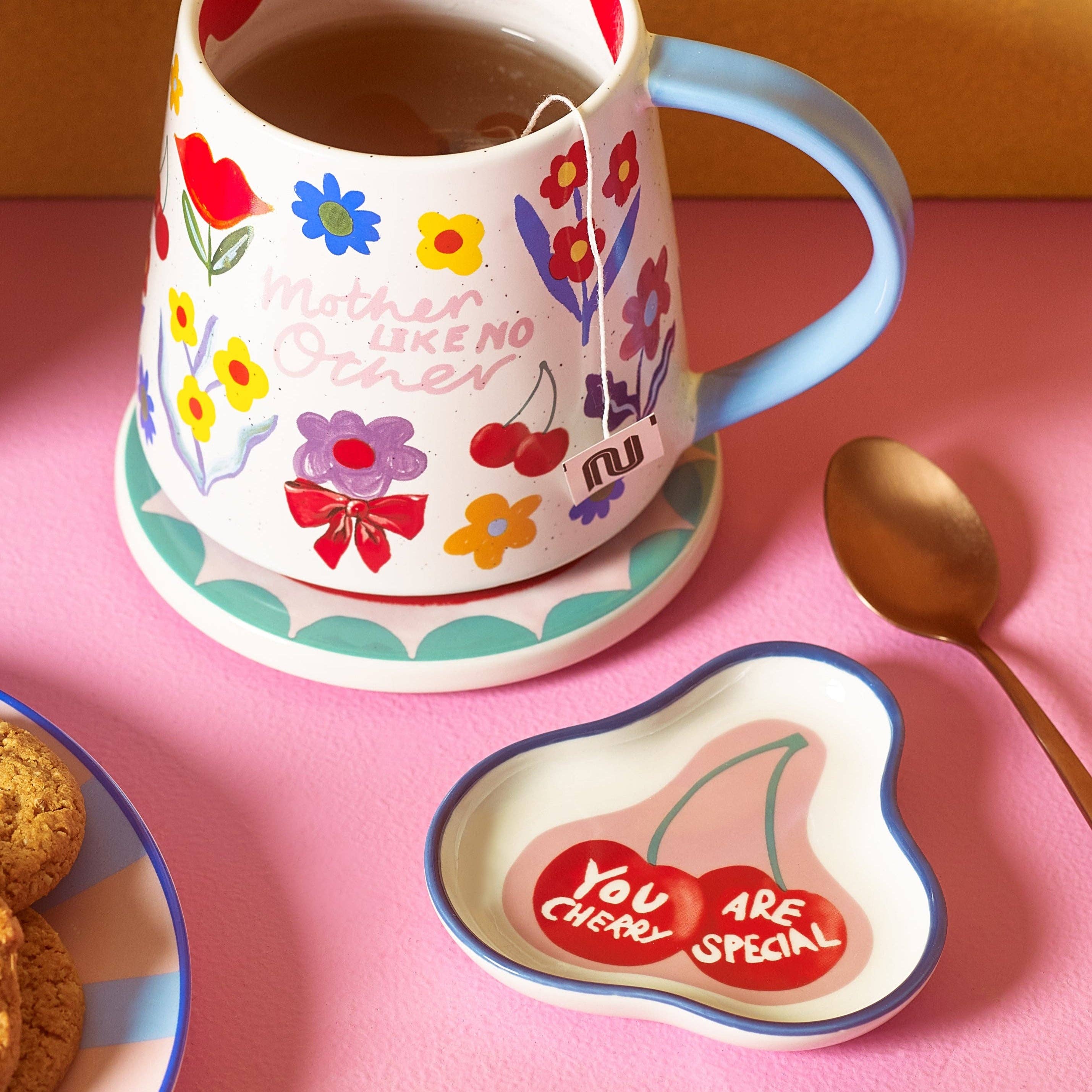 Decorative mug with floral designs and a small plate with 'You are cherry special' message on a pink surface.