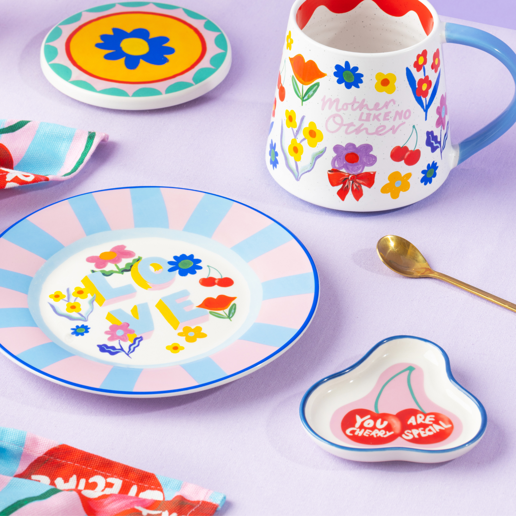 Colorful ceramic items including a mug, plates, and a heart-shaped dish on a light purple background.