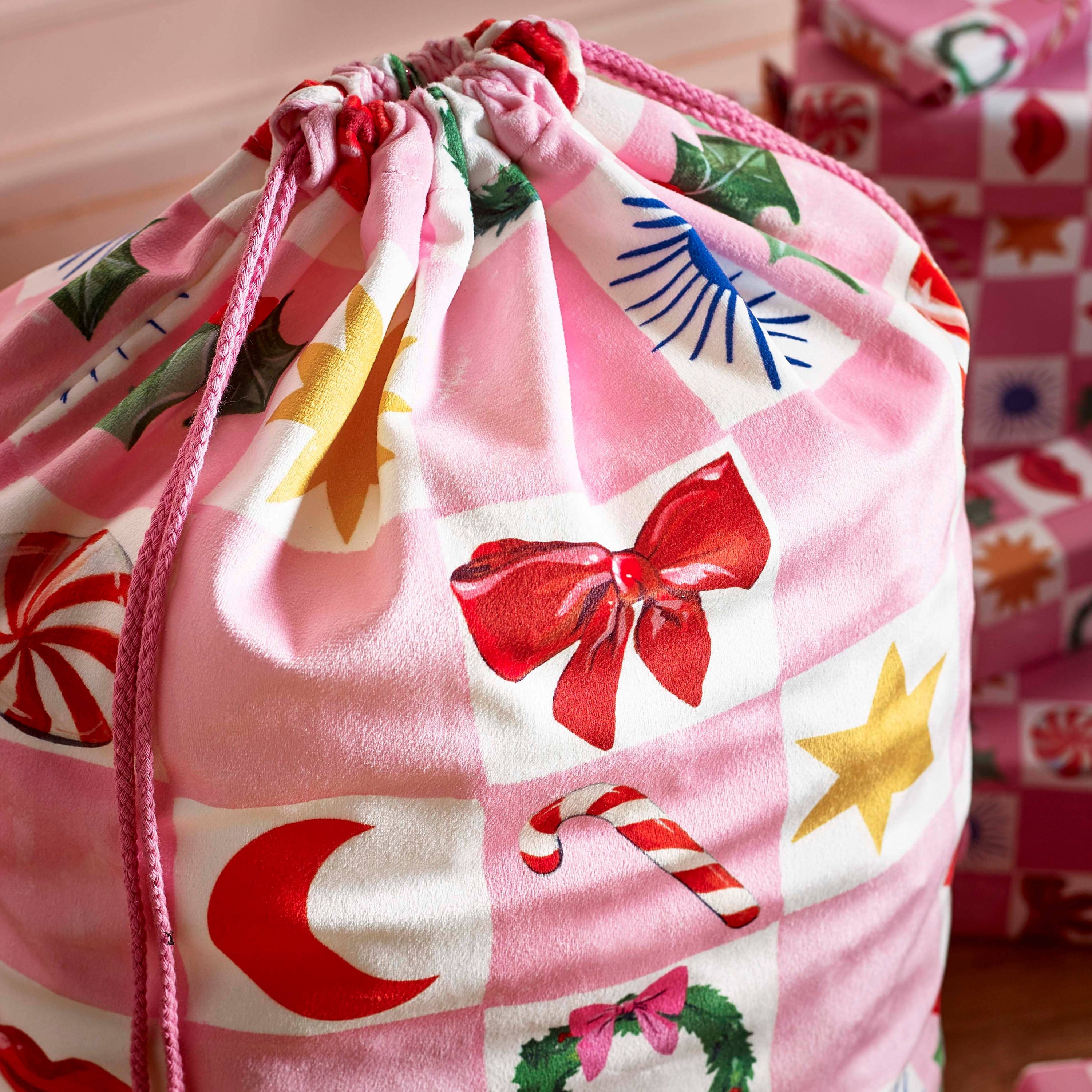 Drawstring bag with Christmas-themed design featuring bows, candy canes, and stars on a pink background.