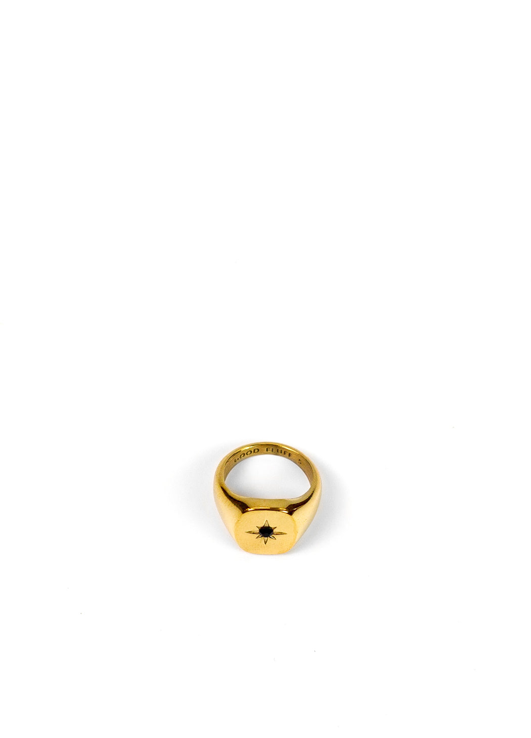 A gold signet ring with a small black star in the center, photographed on a seamless white background.