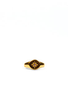 GOLD SIGNET RING WITH STAR GEM AGAINST A WHITE BACKDROP