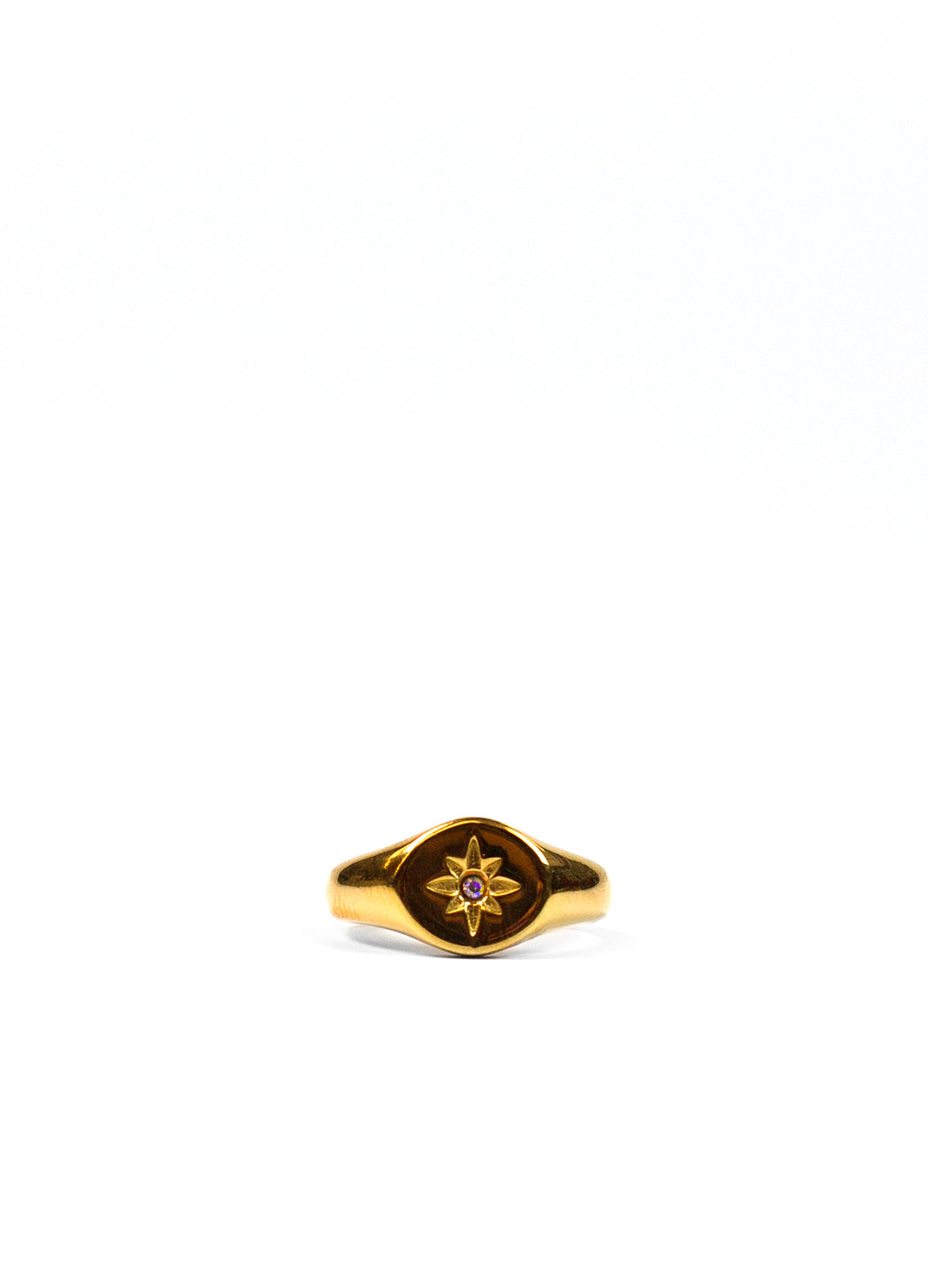 GOLD SIGNET RING WITH STAR GEM AGAINST A WHITE BACKDROP