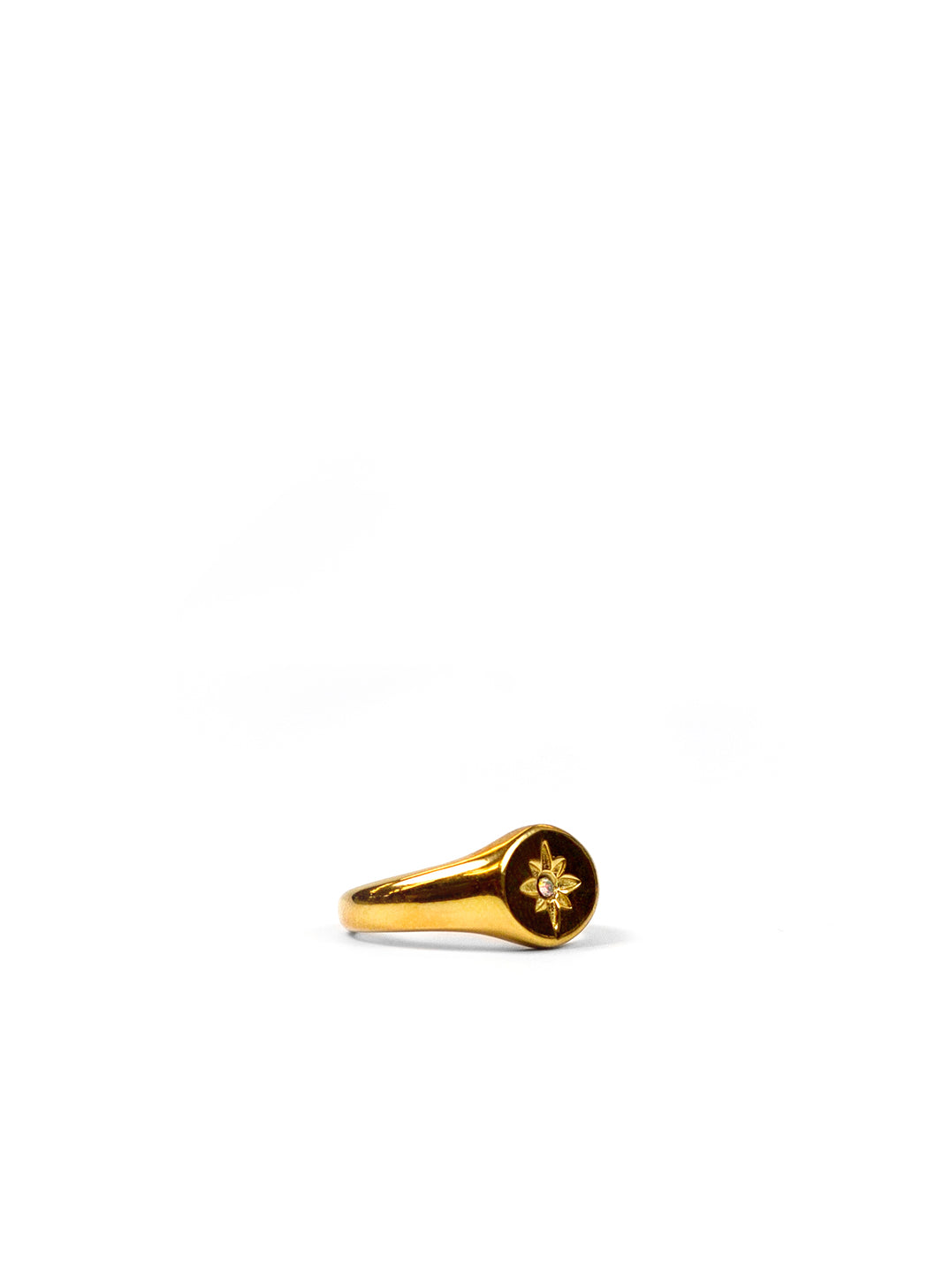 A gold signet ring with a circular face featuring a small gold compass rose motif, photographed on a seamless white background.