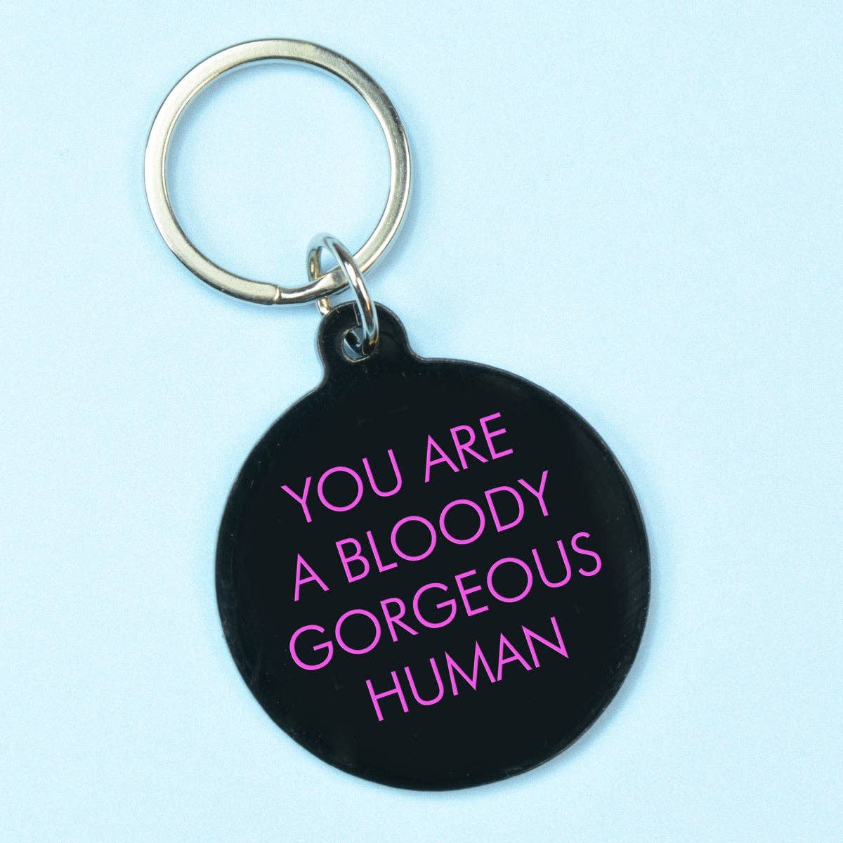 Black keychain with pink text on a light blue background