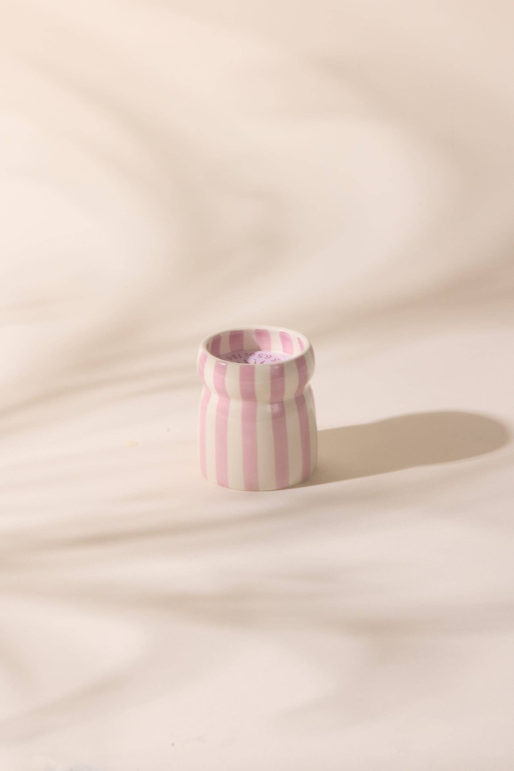 Small pink and white striped ceramic candle on a beige background