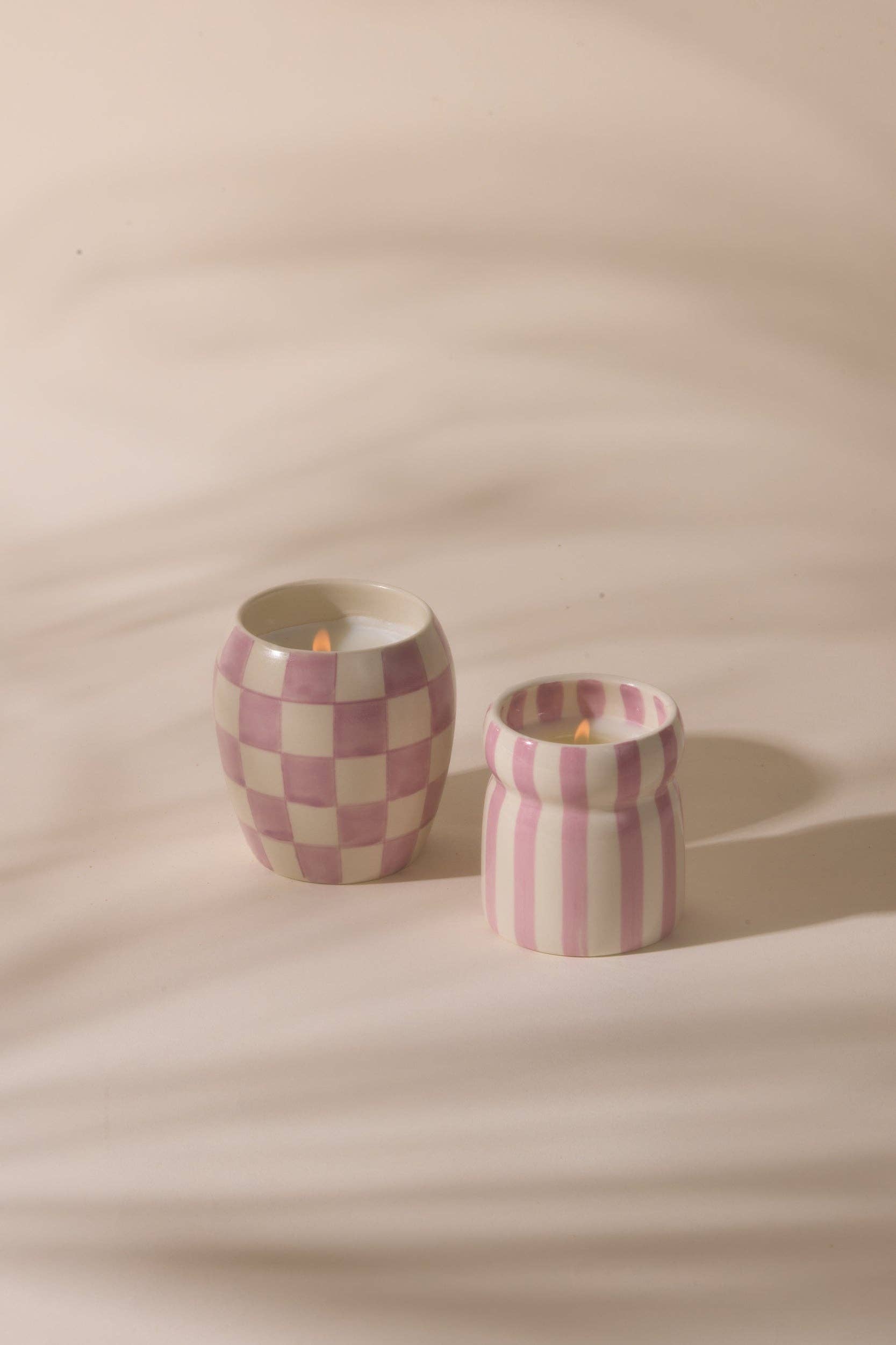 Two checkered ceramic candle holders with candles on a beige background