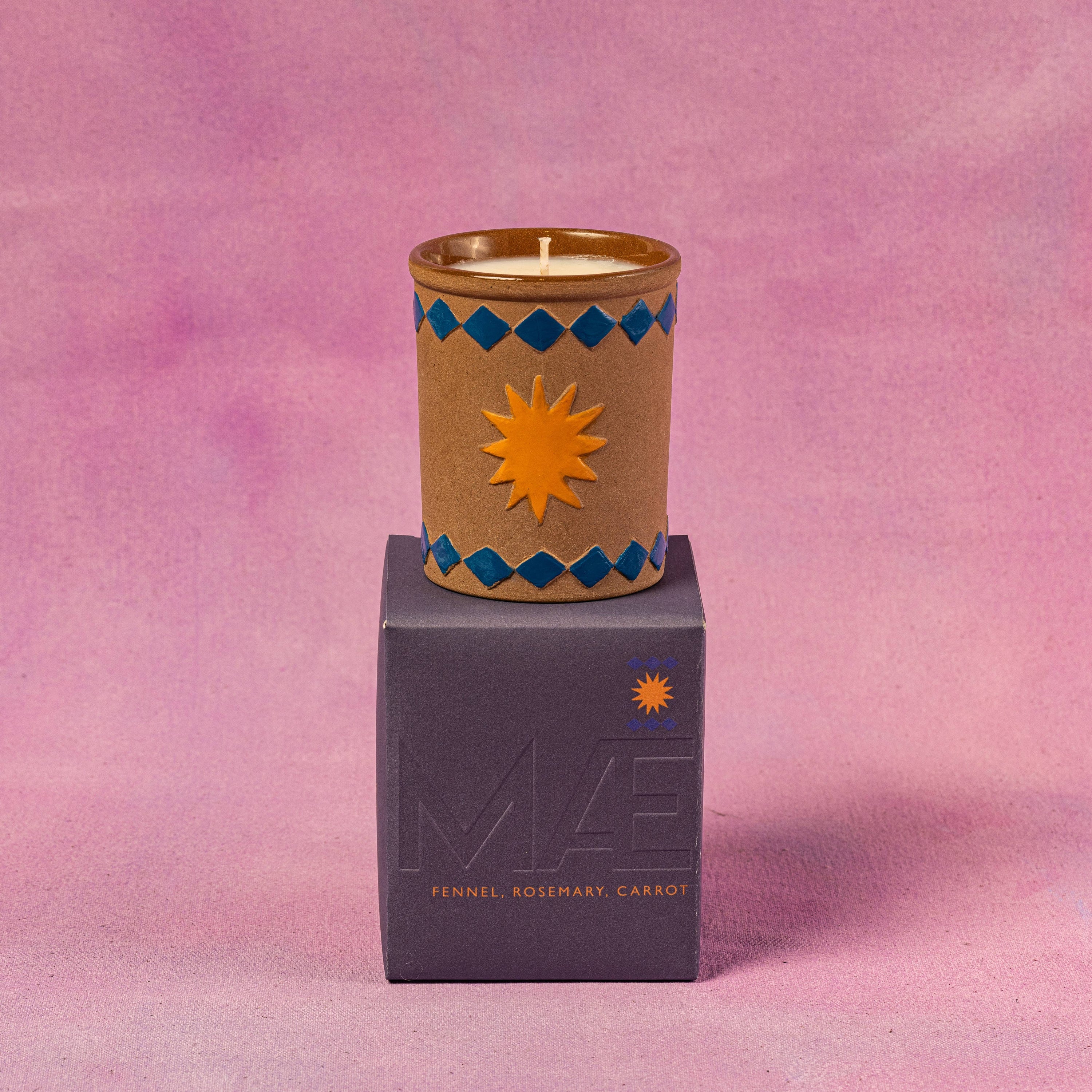 Candle in a decorative container on top of a purple box 