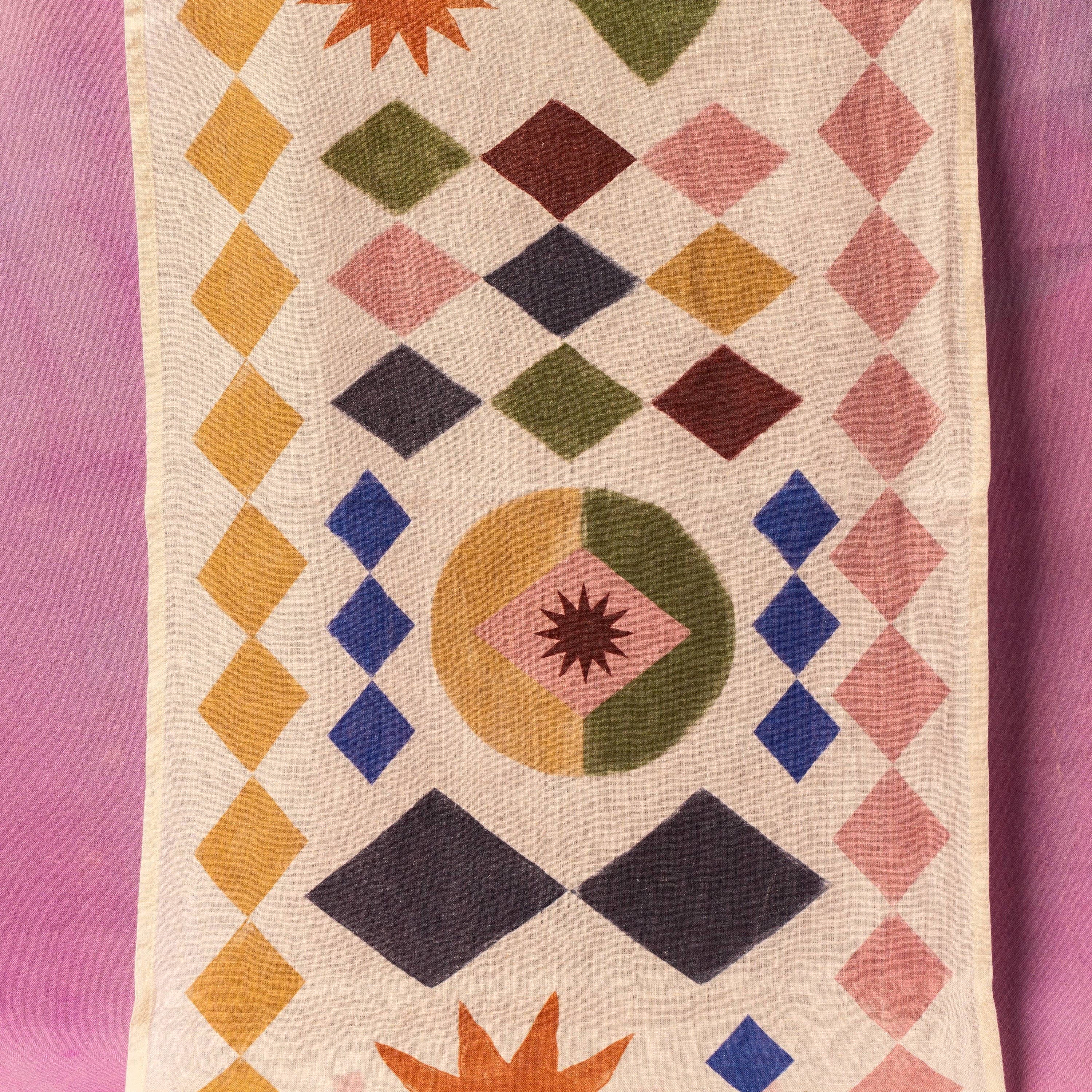 Geometric patterned table runner fabric with colorful shapes on a pink background