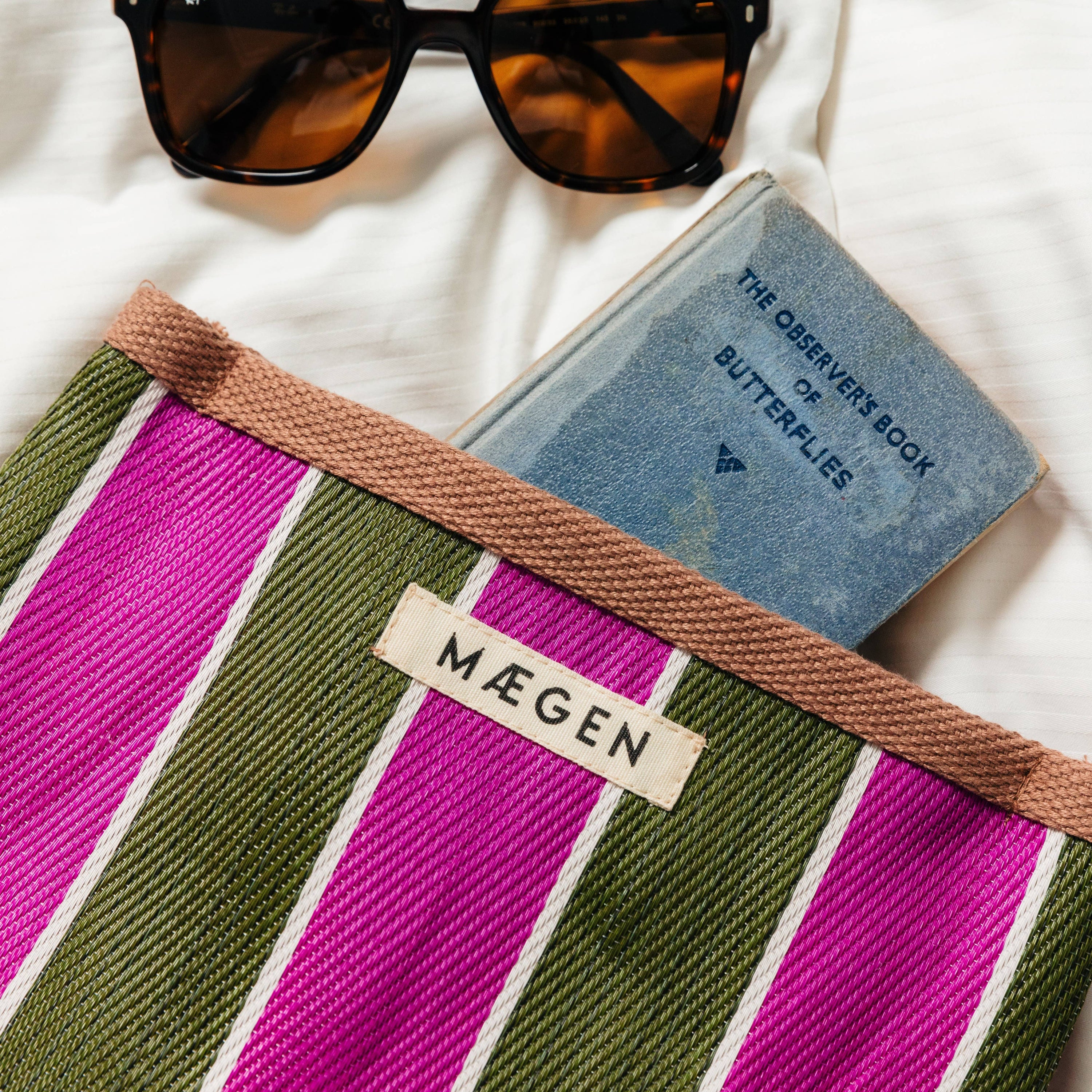 Striped bag with sunglasses and a book on a white background