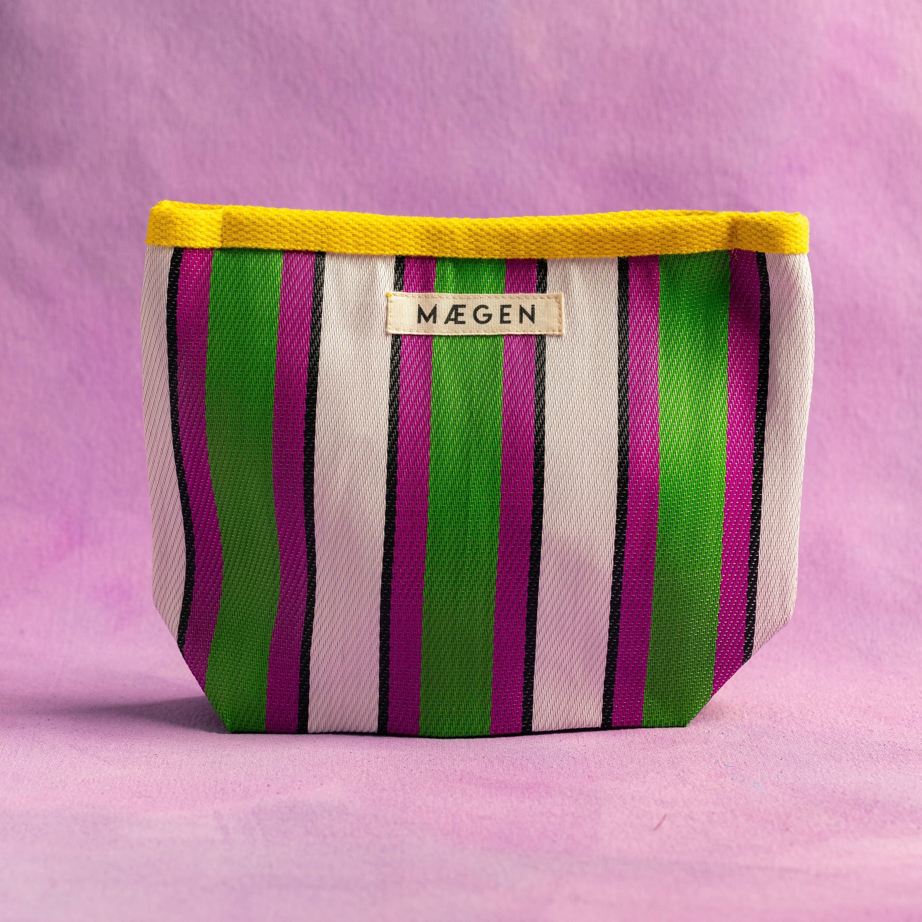 Striped fabric make up bag purse with yellow rim and 'Máegen' label on a pink background