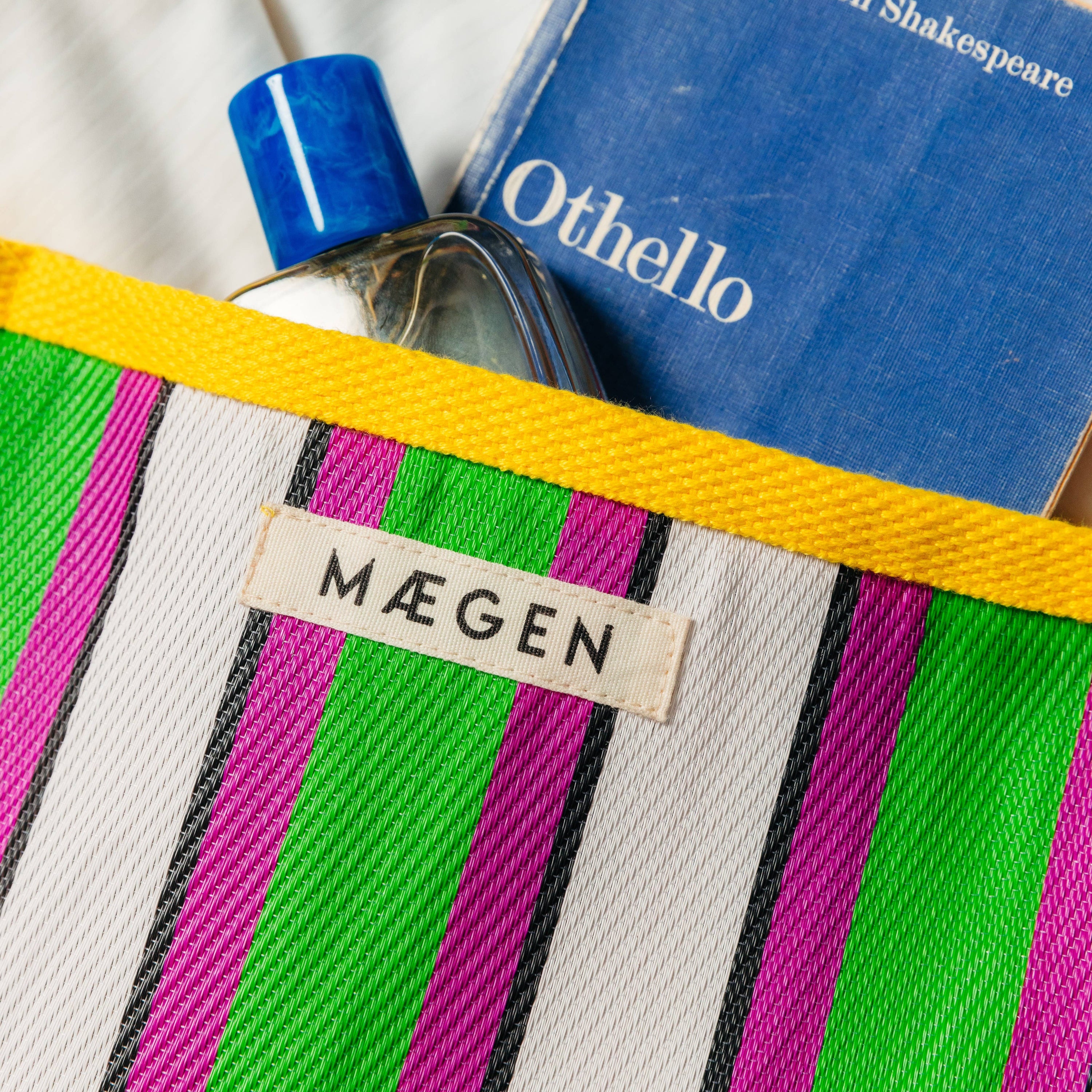 Striped pouch with 'Máegen' label, bottle, and book titled 'Othello' on a white background