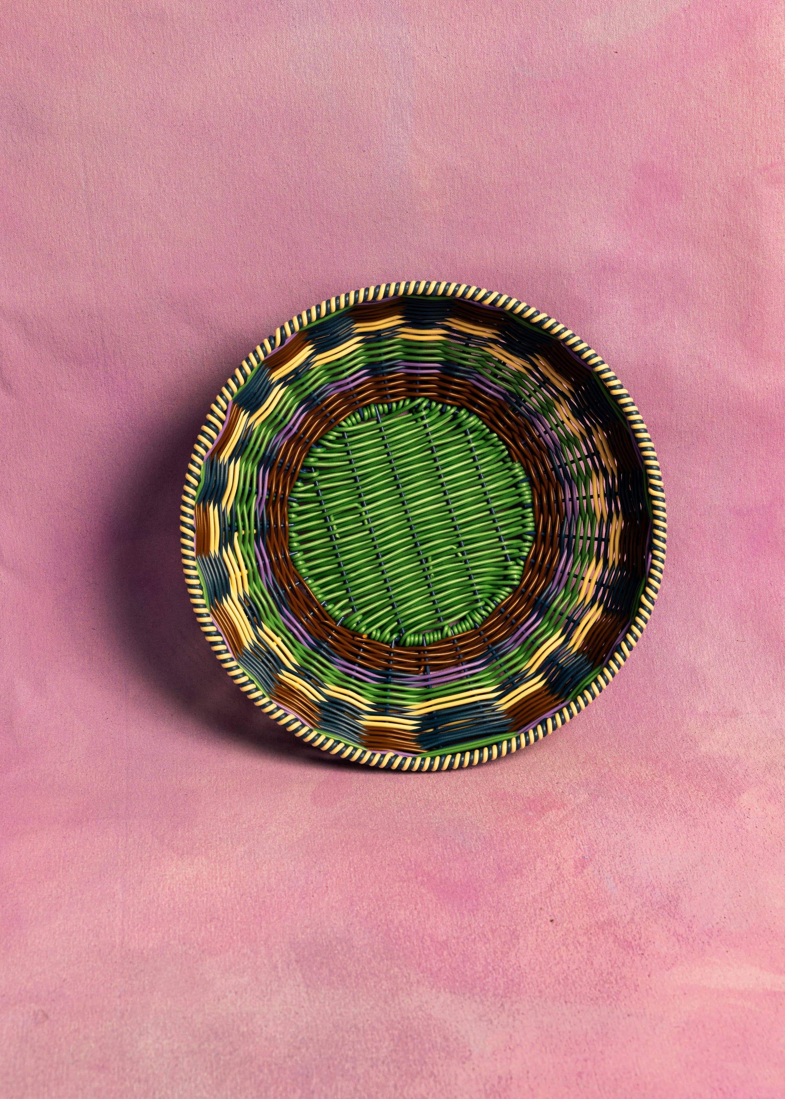 Decorative woven basket with a green center on a pink background