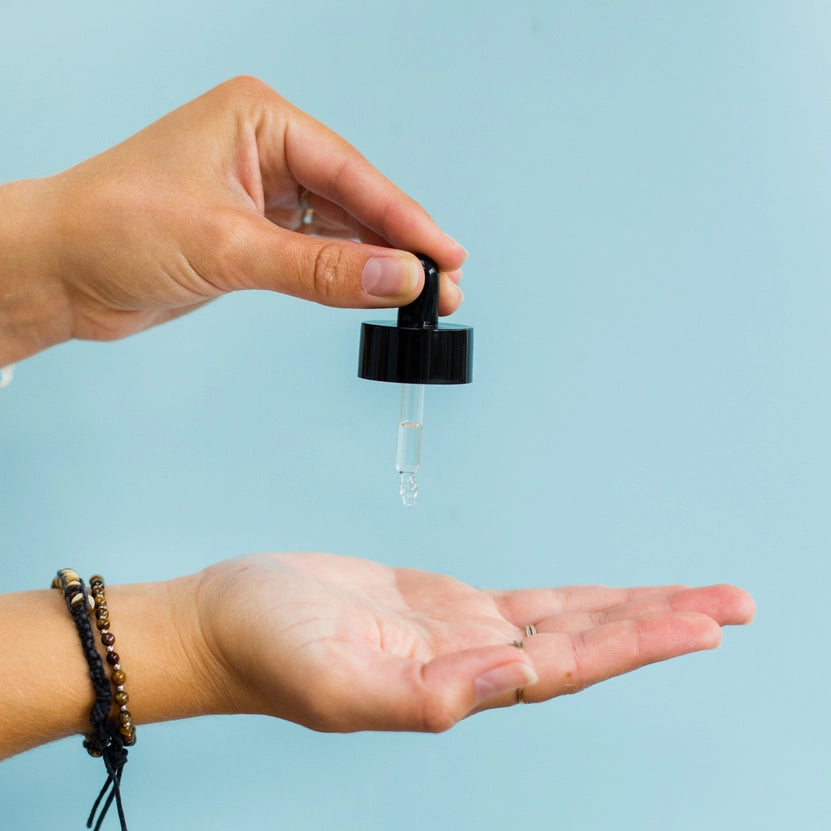 Hand holding a dropper with clear liquid over an open palm against a light blue background