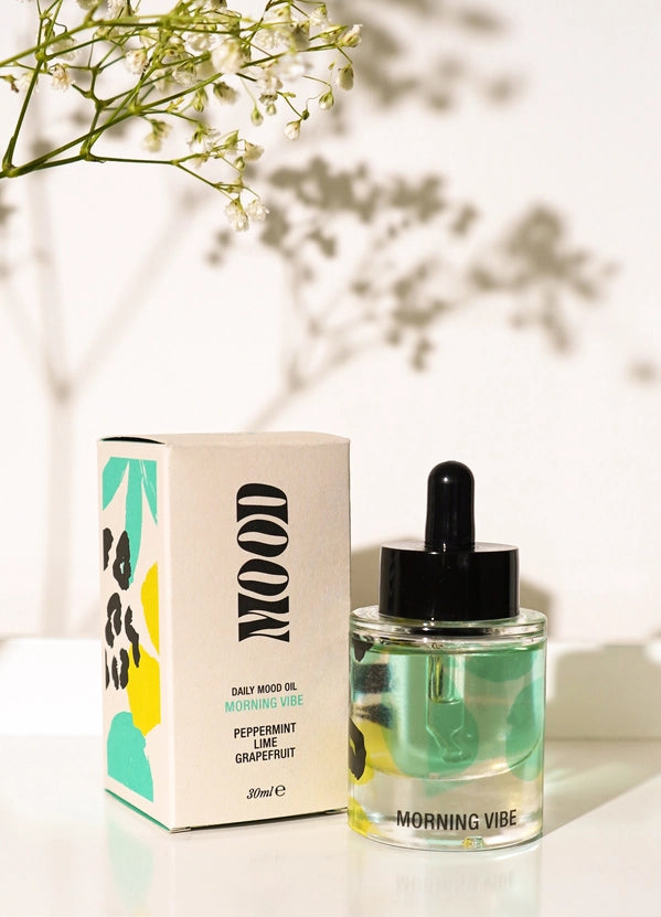 Bottle of 'Morning Vibe' oil with a box on a light surface, blurred greenery in the background