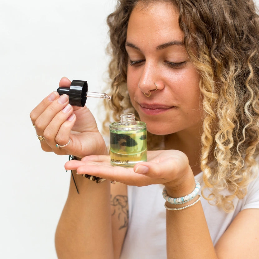 Woman holding a dropper bottle with a clear liquid and a small container labeled 'Vibe' against a white background.