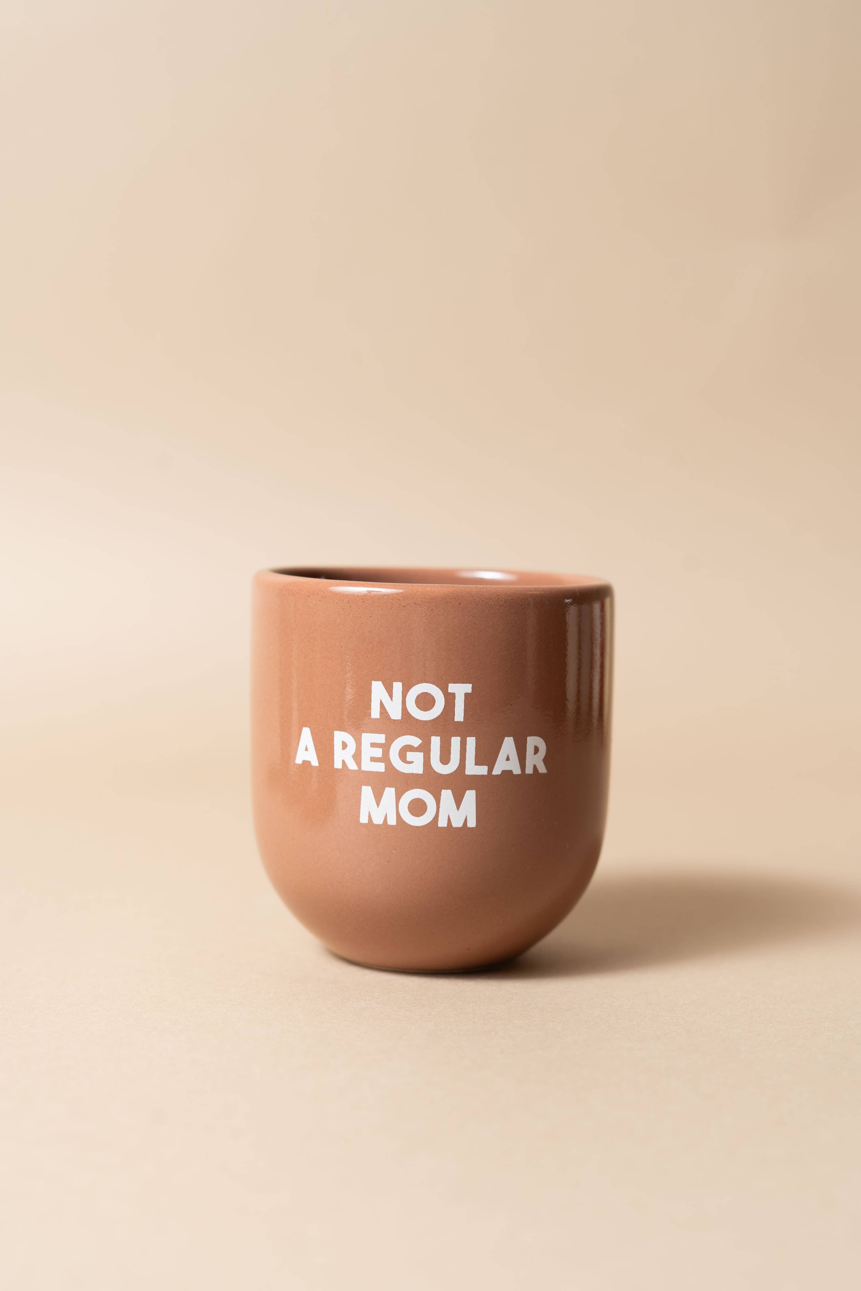 Brown ceramic cup with 'Not a Regular Mom' text on a beige background