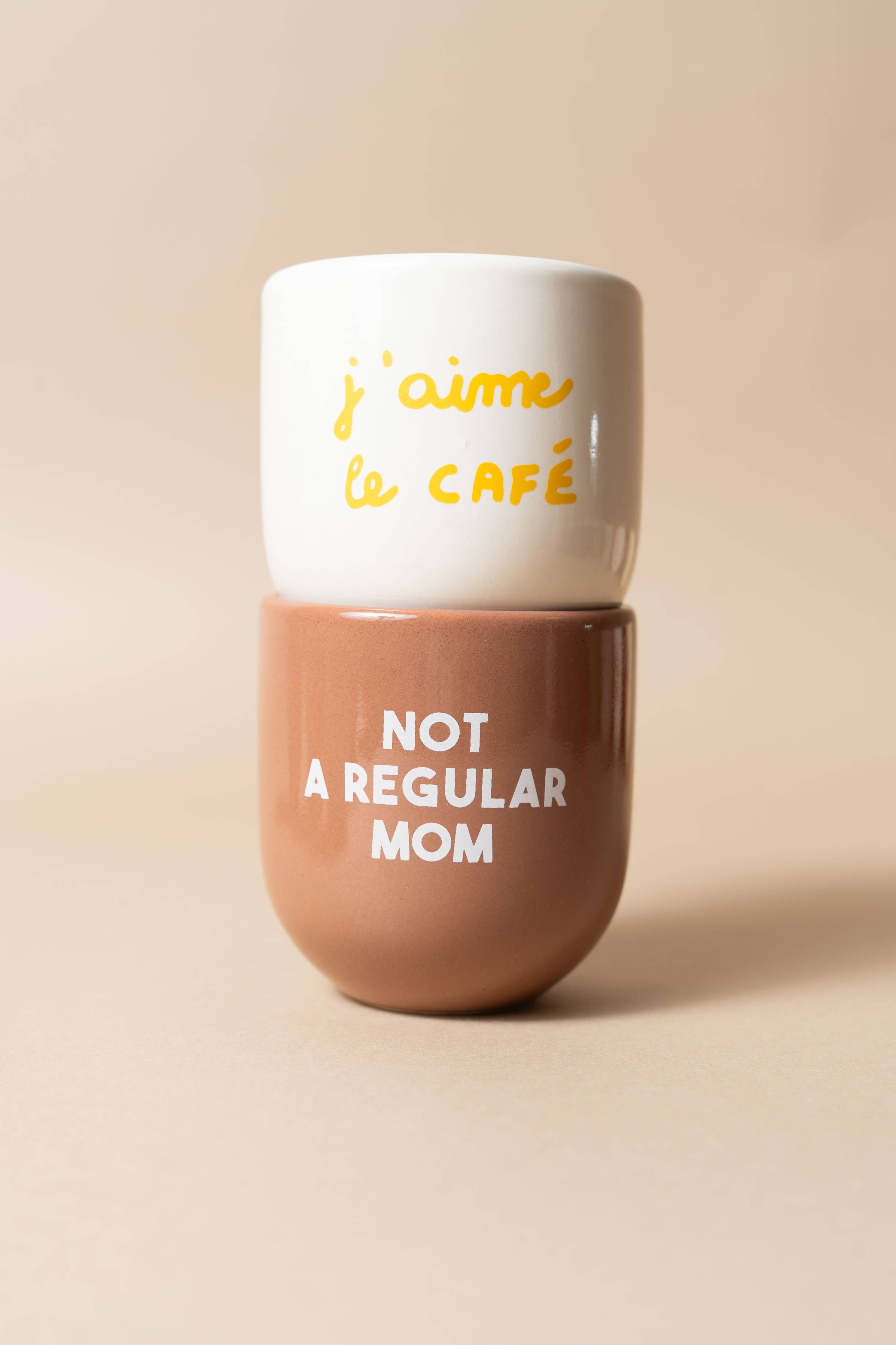 Two-part container with 'j'aime le café' on top and 'Not a Regular Mom' on bottom, on a beige background