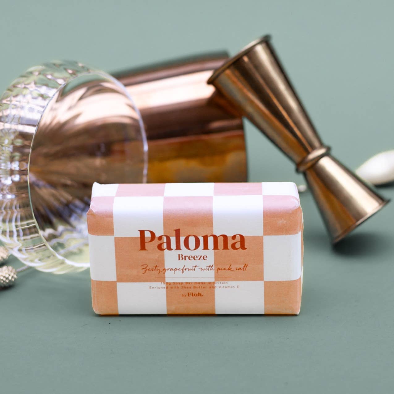 Bar of soap labeled 'Paloma Breeze' with cocktail shakers in the background on a green surface