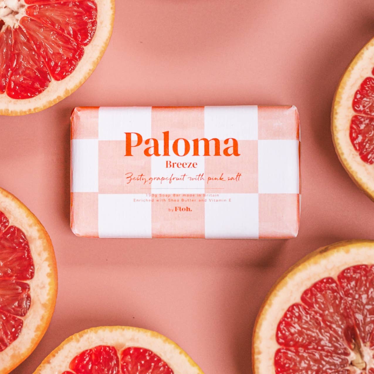 Bar of Paloma Breeze soap with checkered design surrounded by grapefruit slices on a pink background