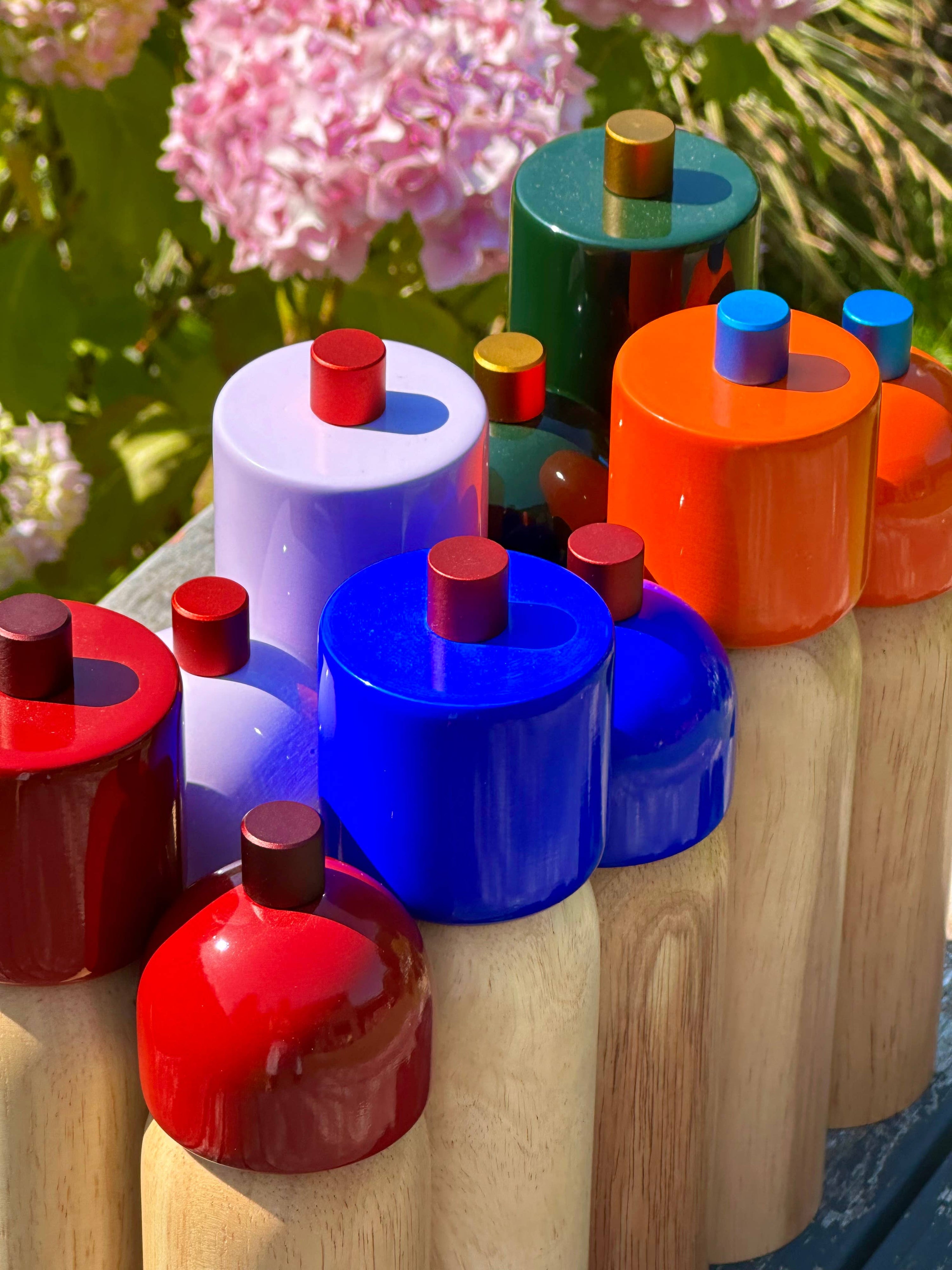 Colorful cylindrical objects on a wooden surface with flowers in the background