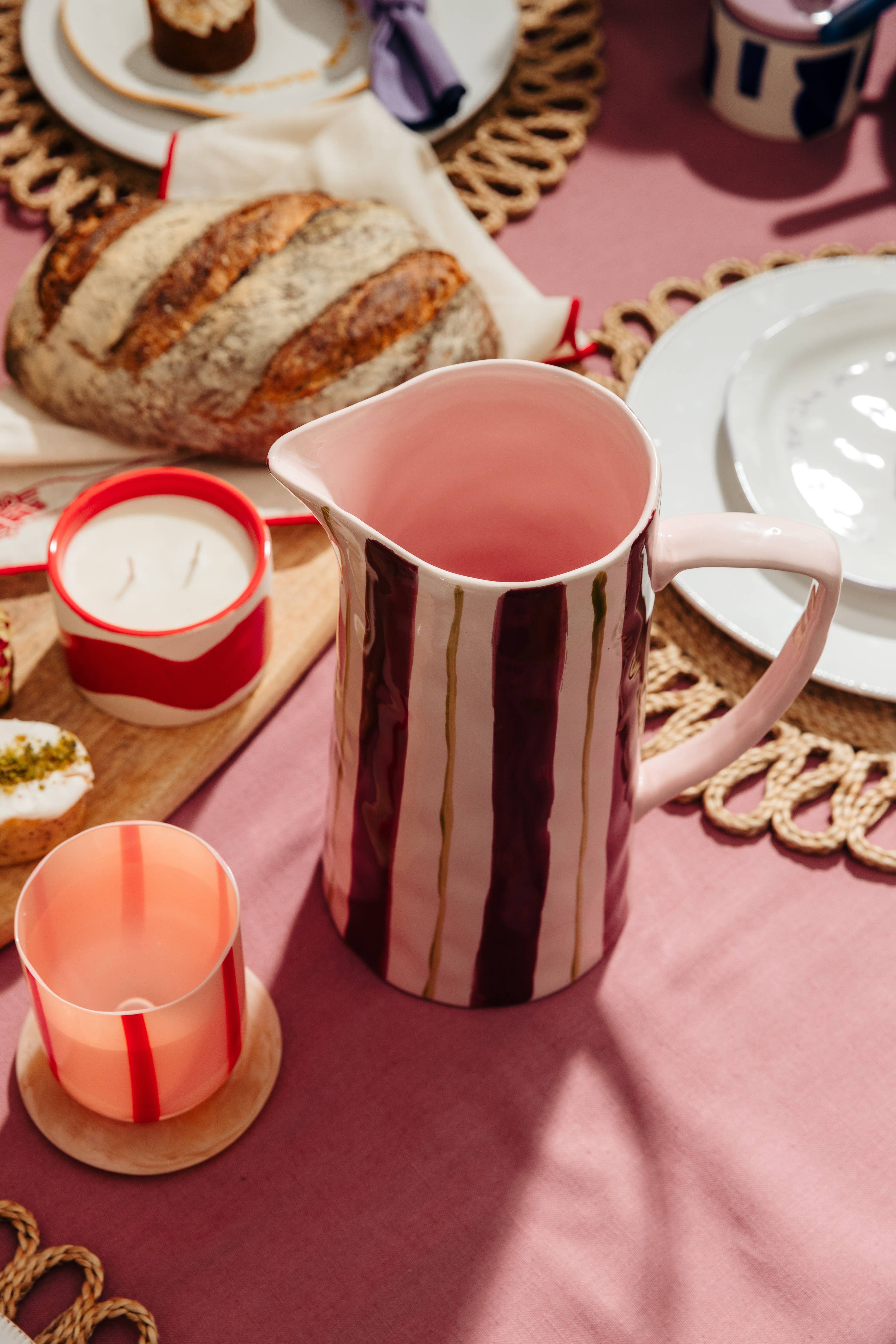 Pink and brown striped pitcher on a pink tablecloth with bread and candles.