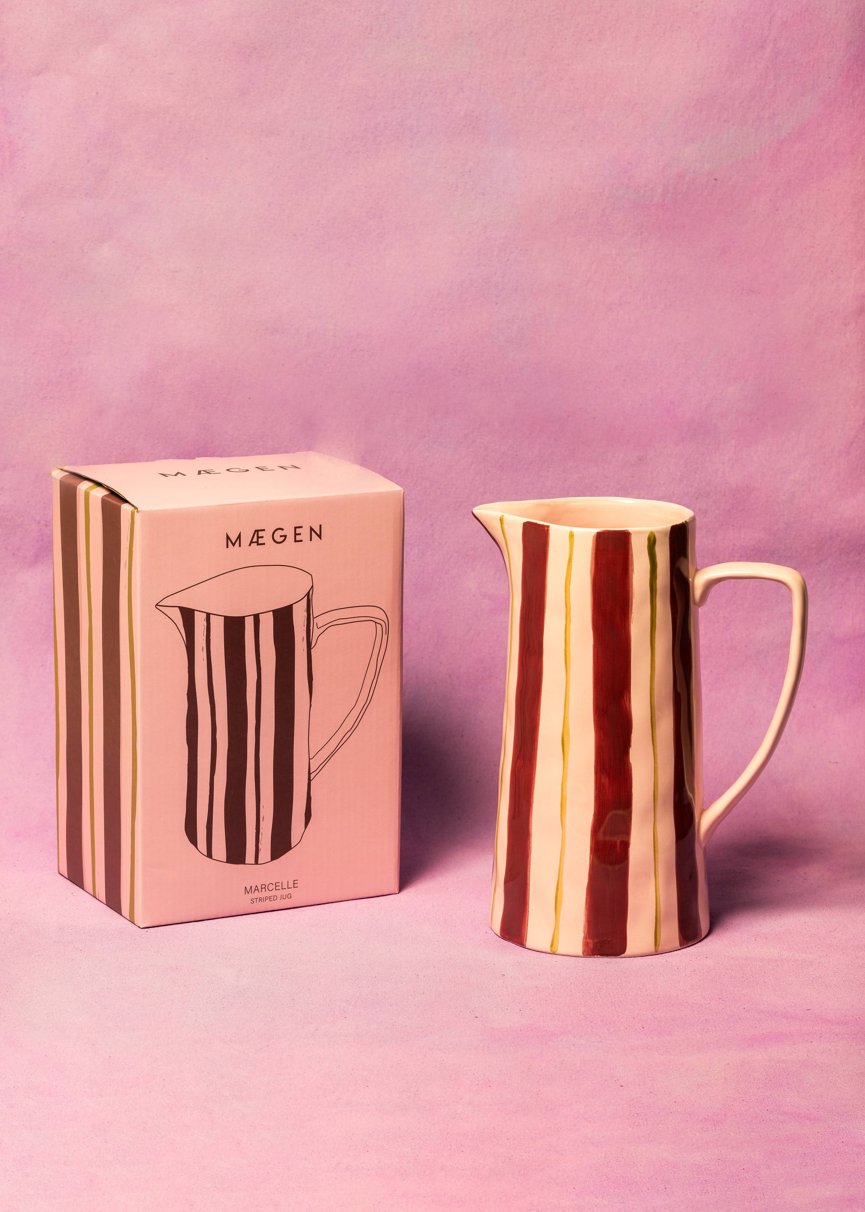 Rose gold pitcher with striped design next to its packaging on a pink background