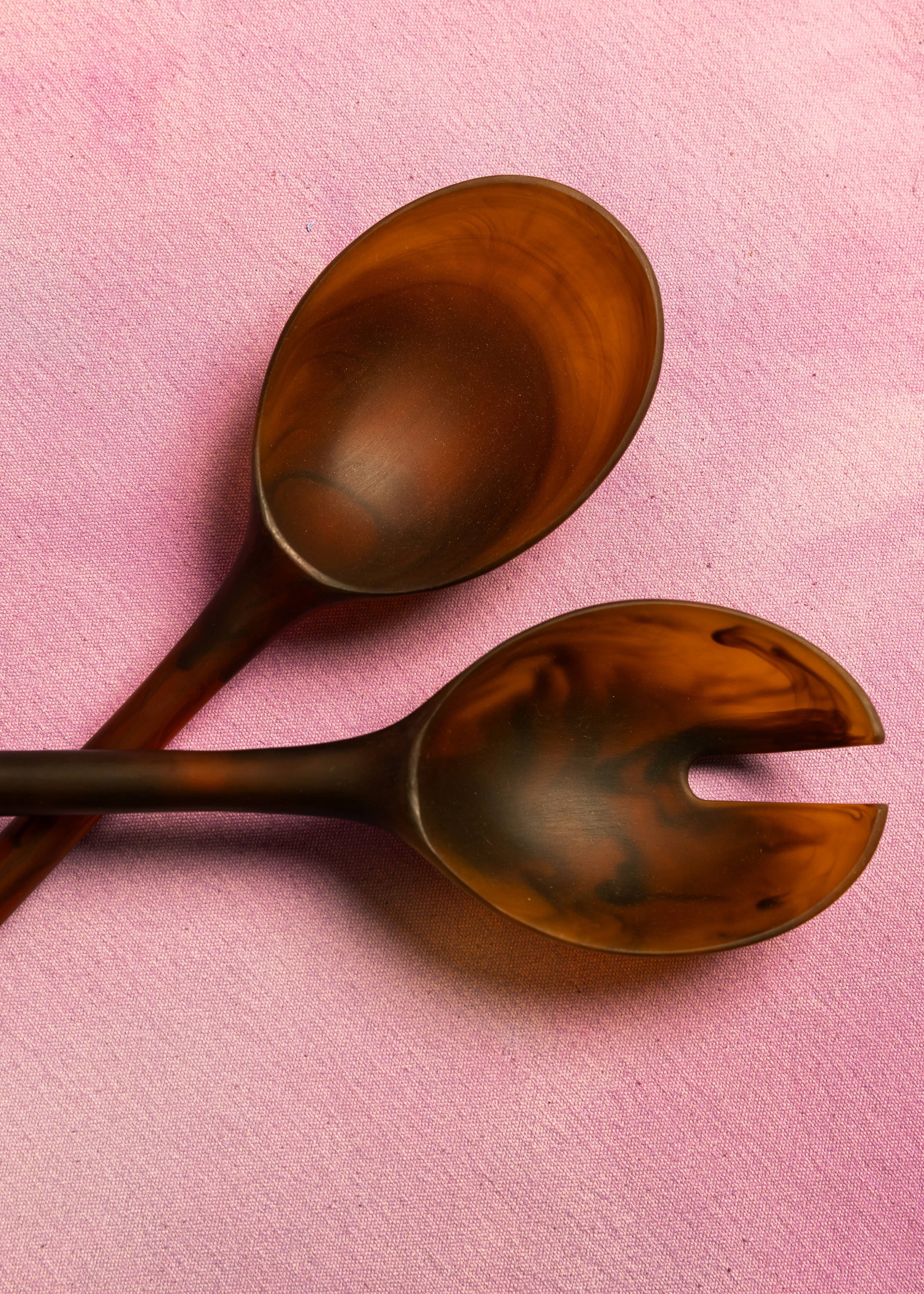 Two wooden salad servers on a pink background