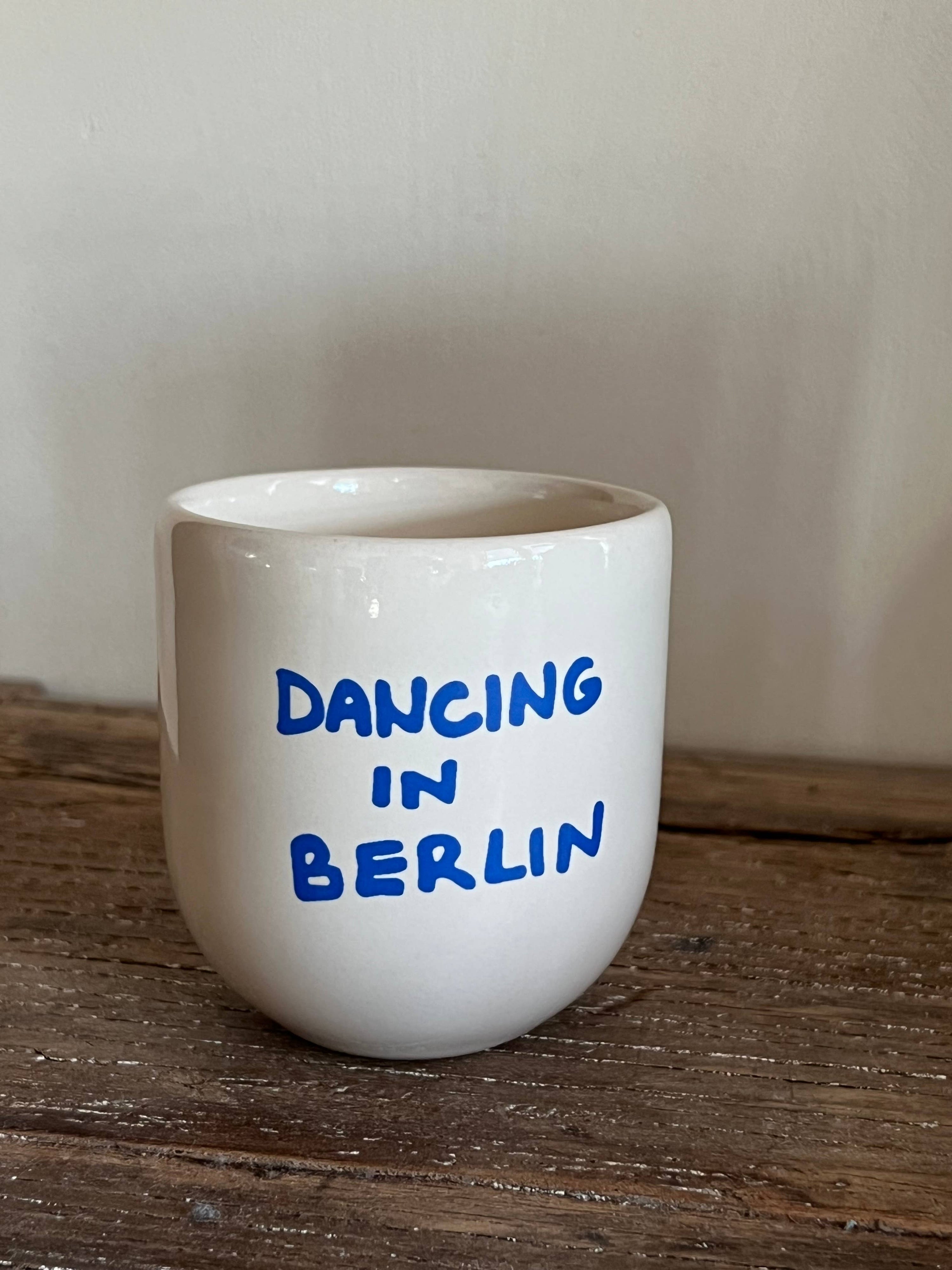 White ceramic cup with 'Dancing in Berlin' text on a wooden surface