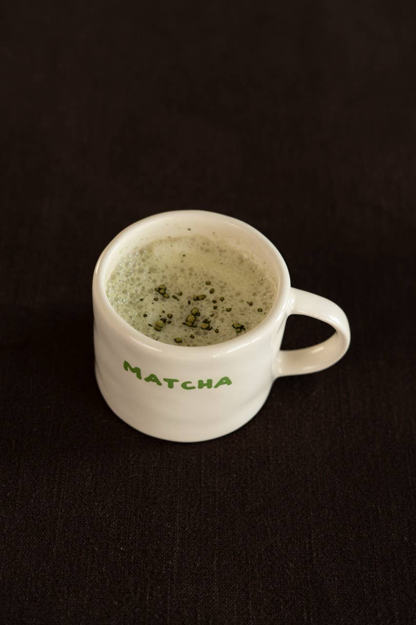 White mug with 'Matcha' text containing matcha green tea on a black background