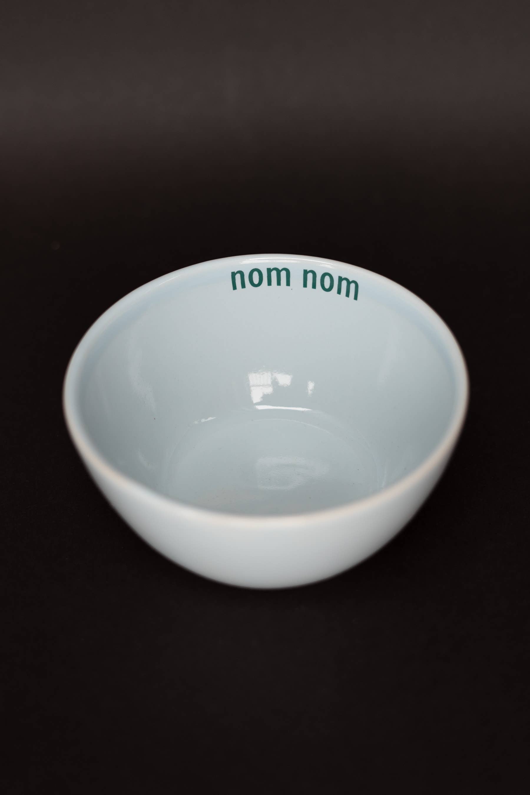 Blue bowl with green 'nom nom' text on a black background