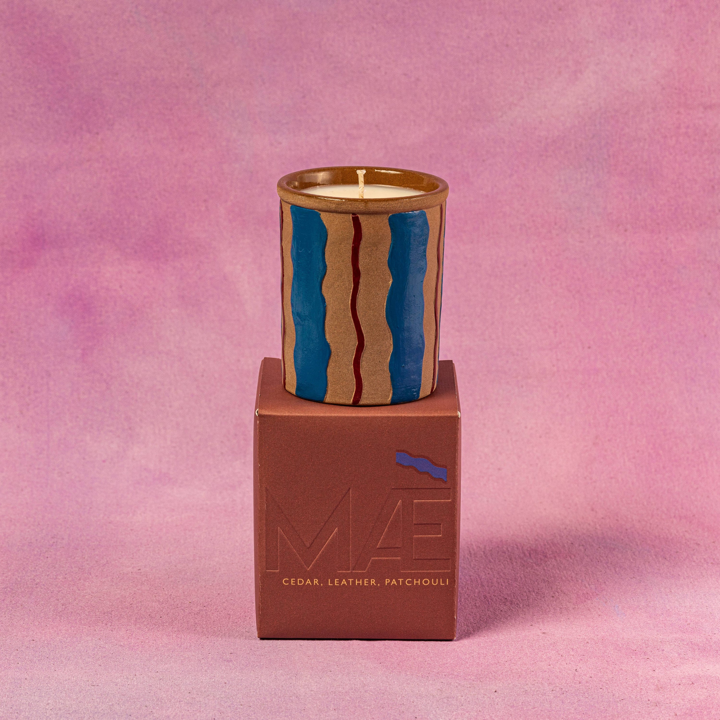 Candle in a CERAMIC WAVY container on top of a brown box 