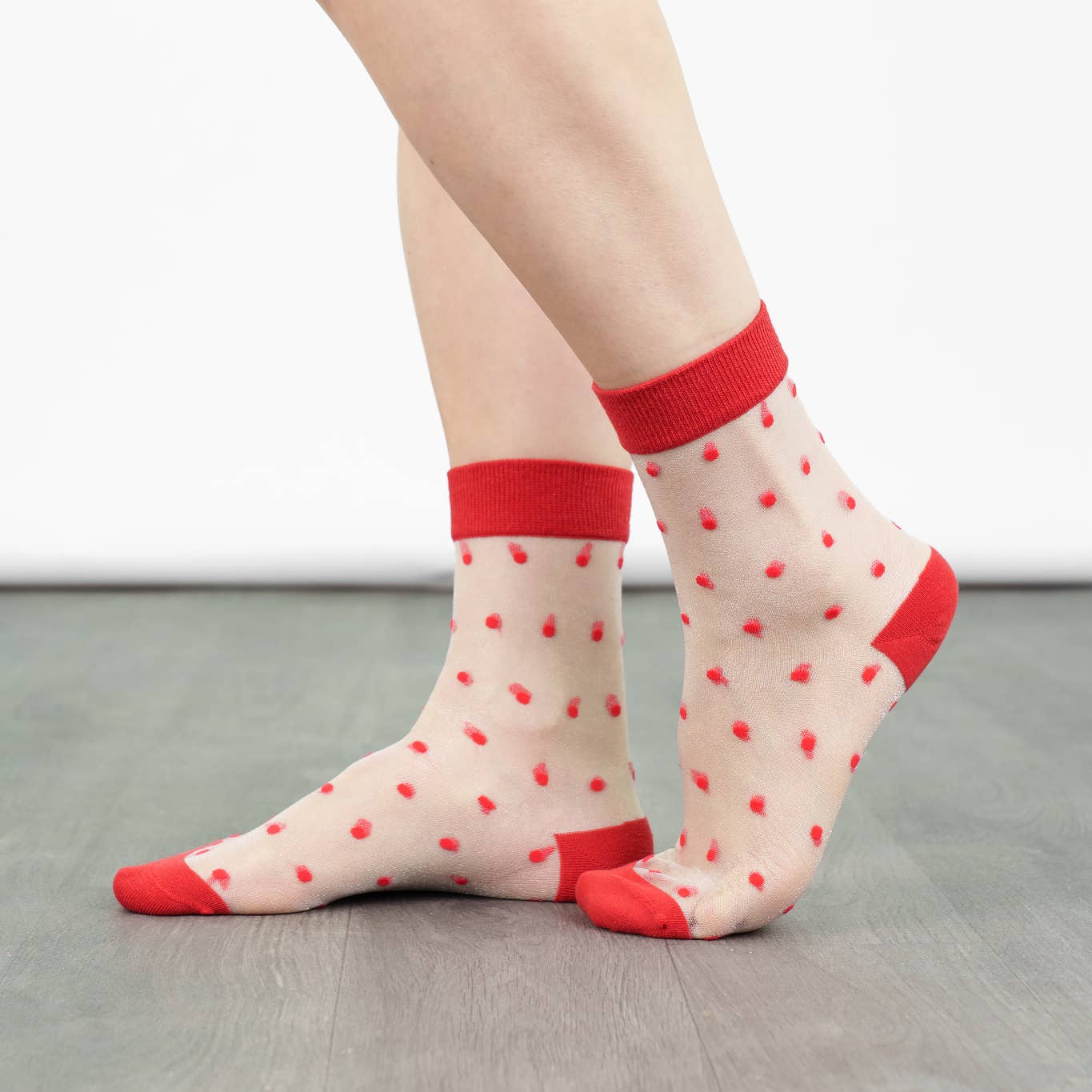 Transparent socks with red heart patterns and red cuffs and toes worn by a person.