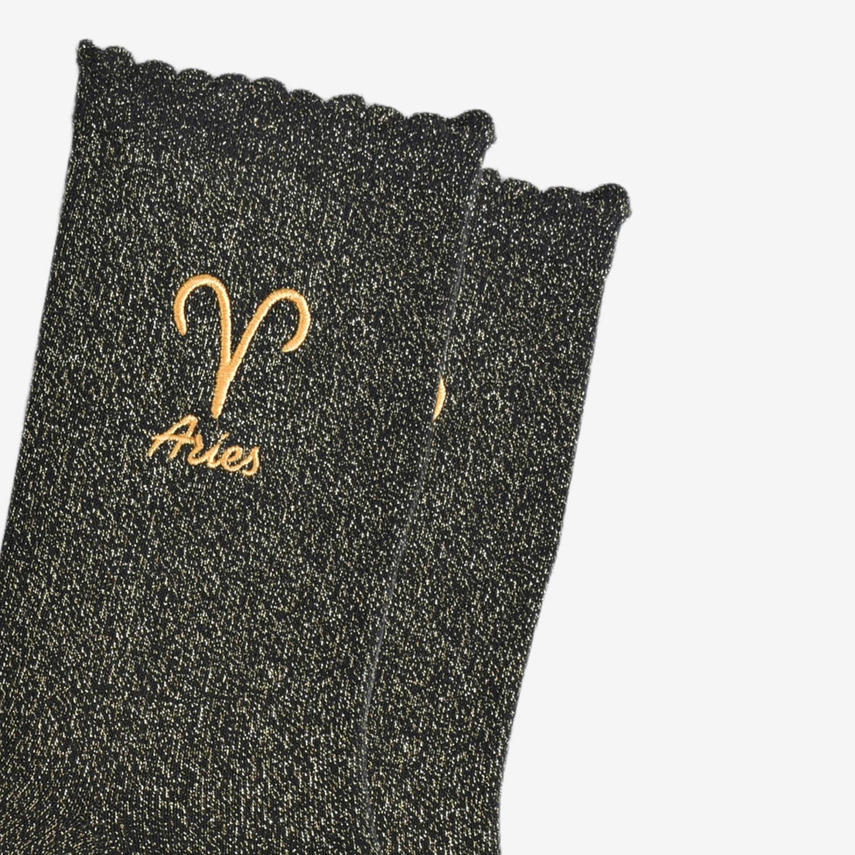 Black glittery sock with 'Aries' embroidered on it against a white background
