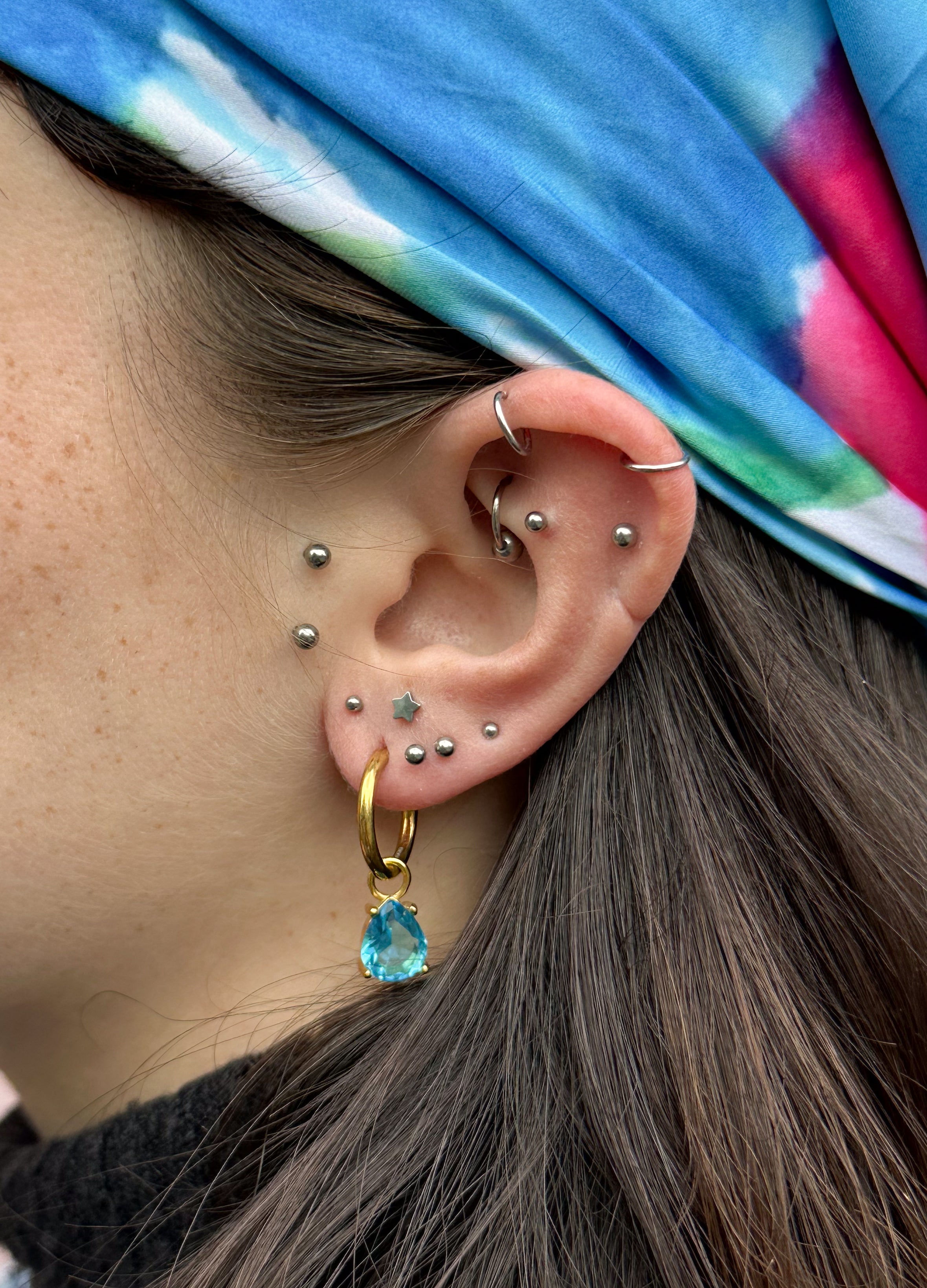 Close-up of a models ear with multiple piercings and the good fluff birthstone huggy earrings.