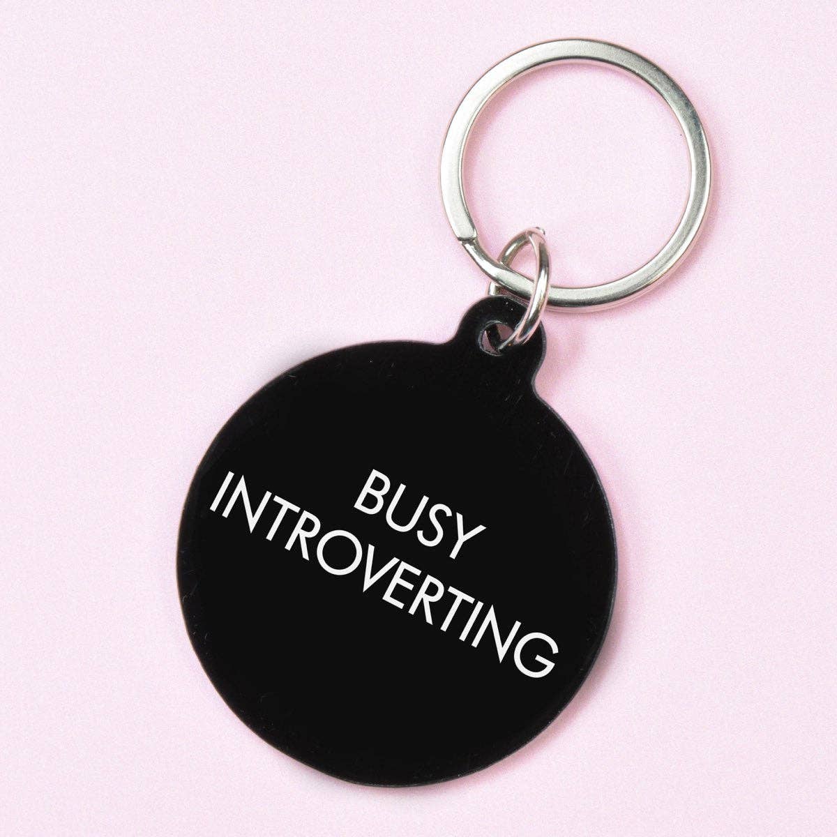 Black keychain with 'BUSY INTROVERTING' text on a pink background